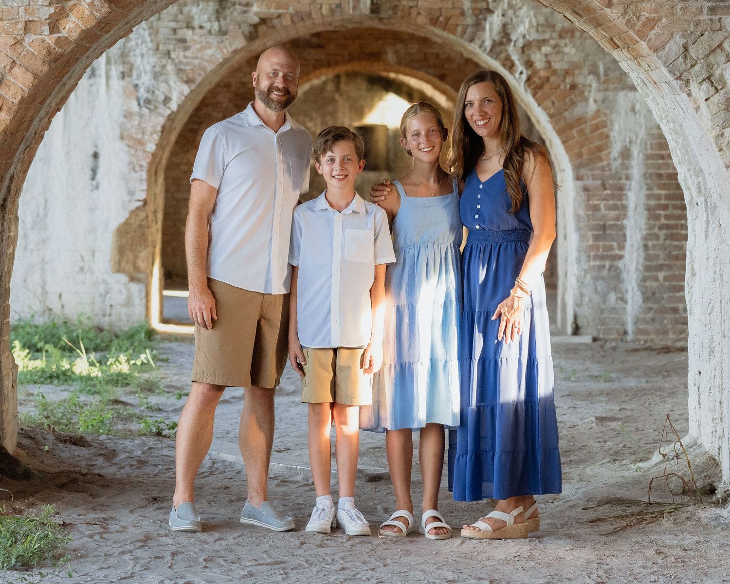 Family of four smiling under brick arches at a historic fort during a sunny outdoor photo session.