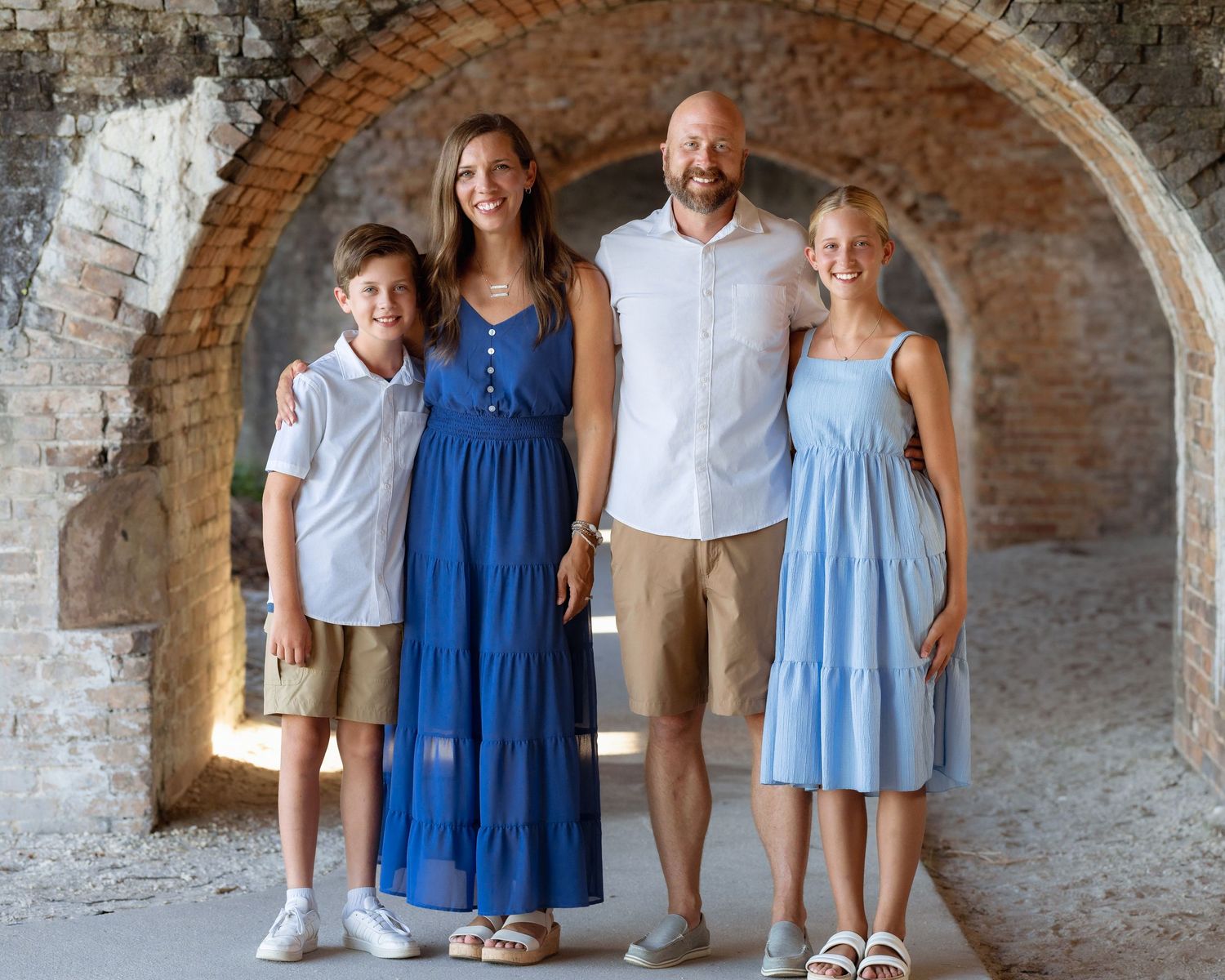 Family of four smiling under stone arches, wearing coordinating blue and white outfits.