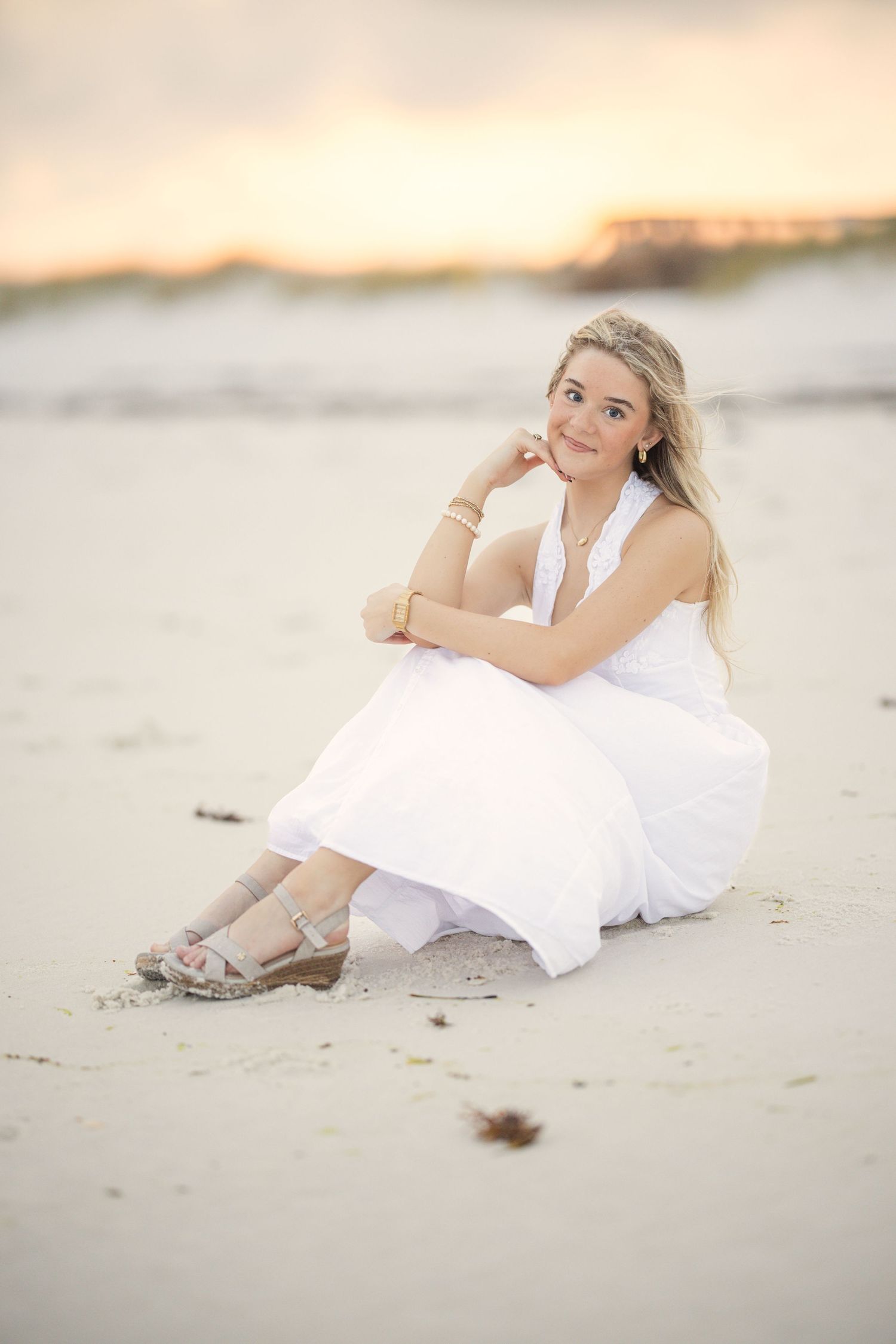 A white sundress photoshoot at sunset on a peaceful beach with soft lighting and sandy backdrop.