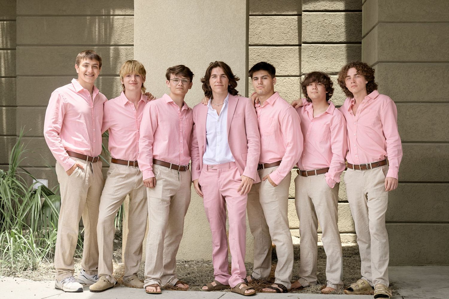 Wedding group photo featuring matching pink shirts and khaki pants against neutral backdrop.