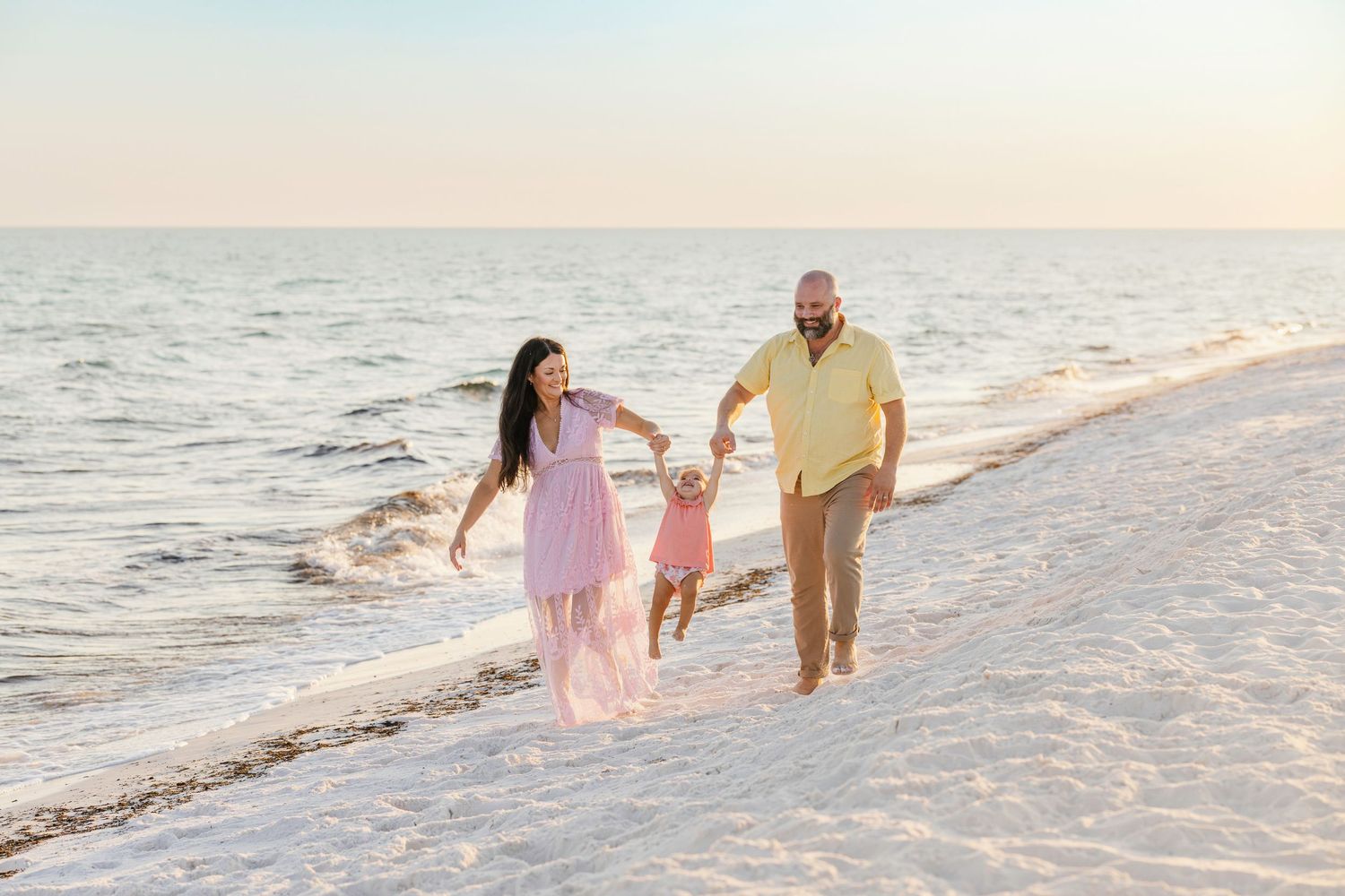 A family taking a sunset stroll along a white sandy beach with gentle waves rolling in at the shoreline.