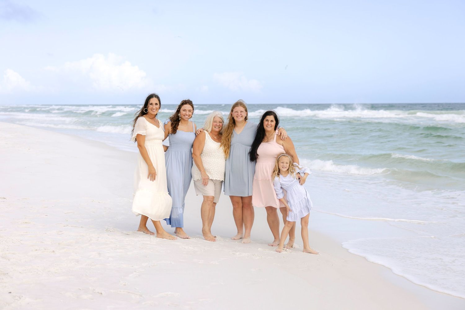 Group enjoying a sunny day walking together along a white sandy beach with ocean waves in the background.