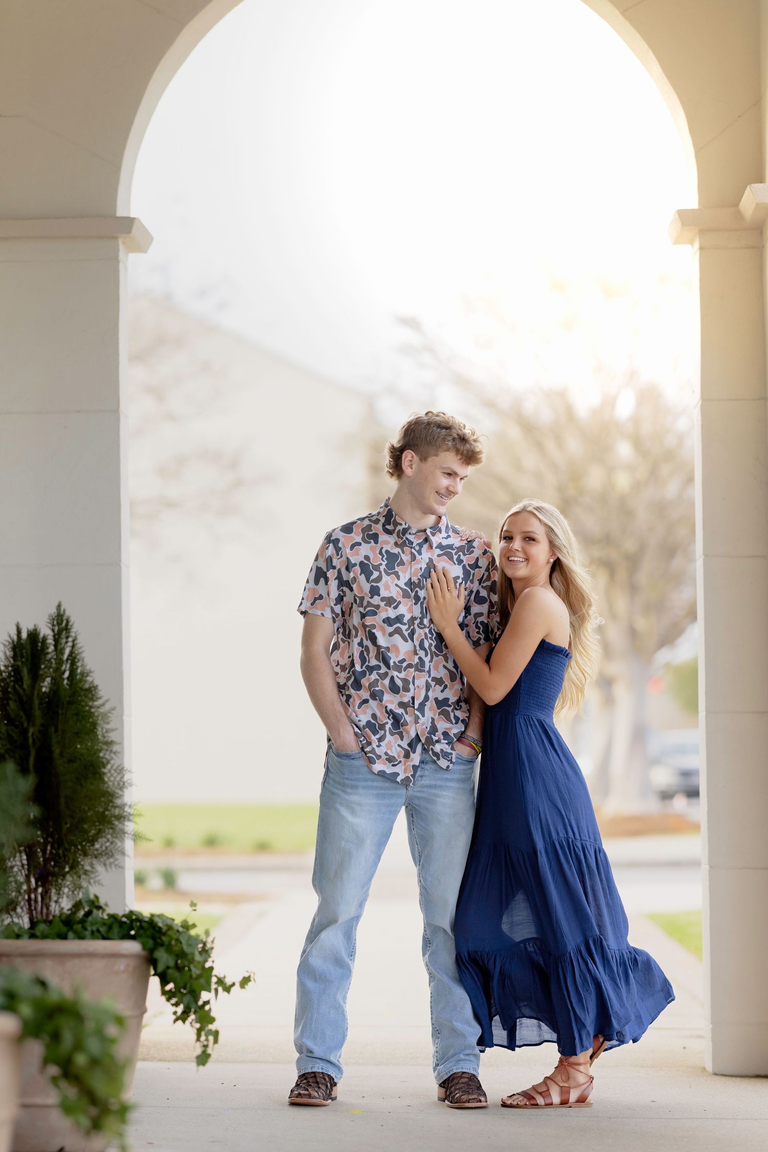 A couple in coordinating blue outfits share romantic moments under a white columned portico.