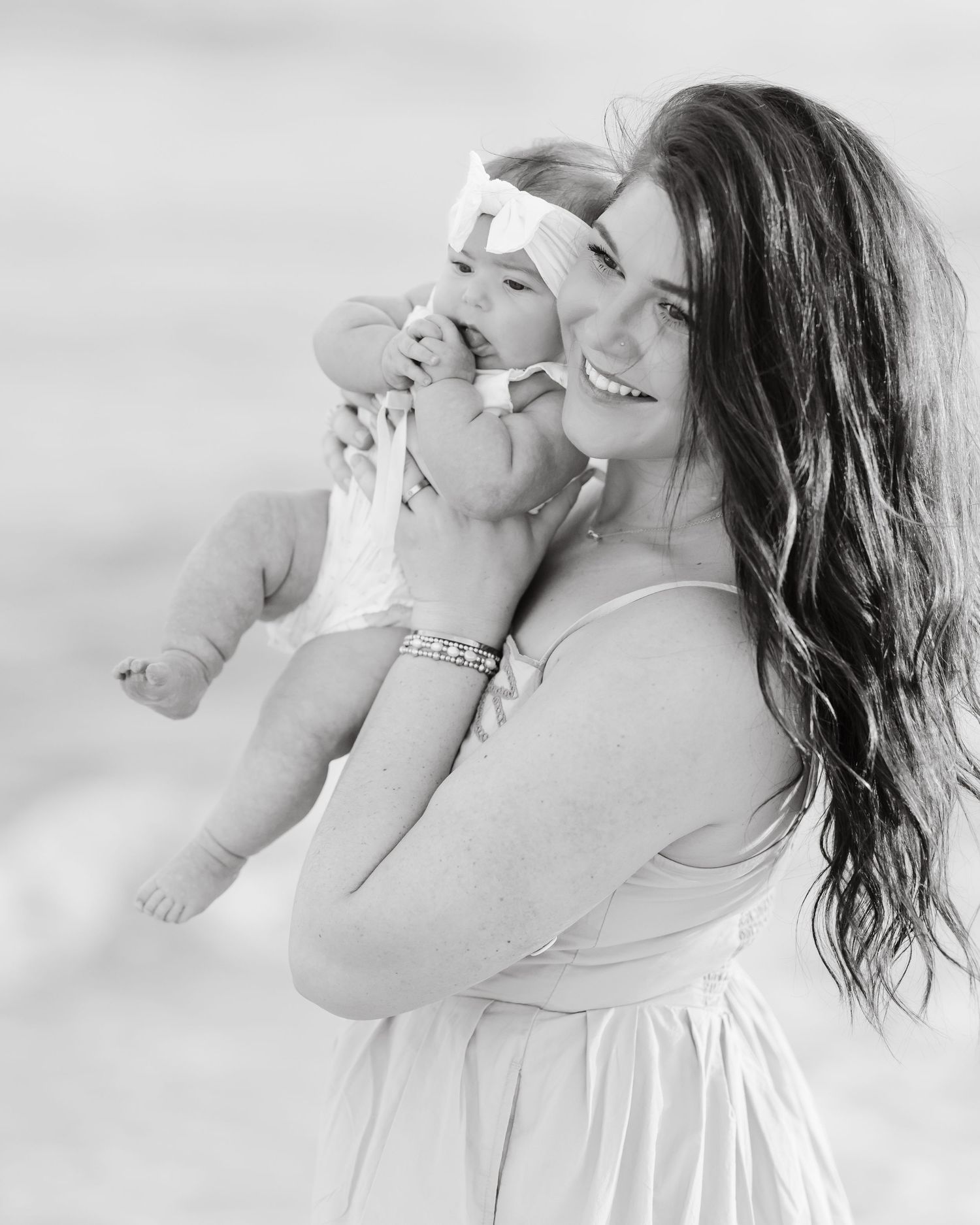 Black and white photo of a smiling mother holding her baby on the beach.