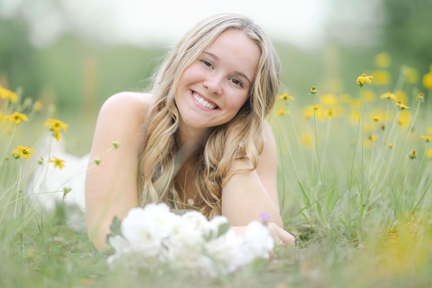 Person in a white dress lies in a field of yellow wildflowers on a sunny summer day.