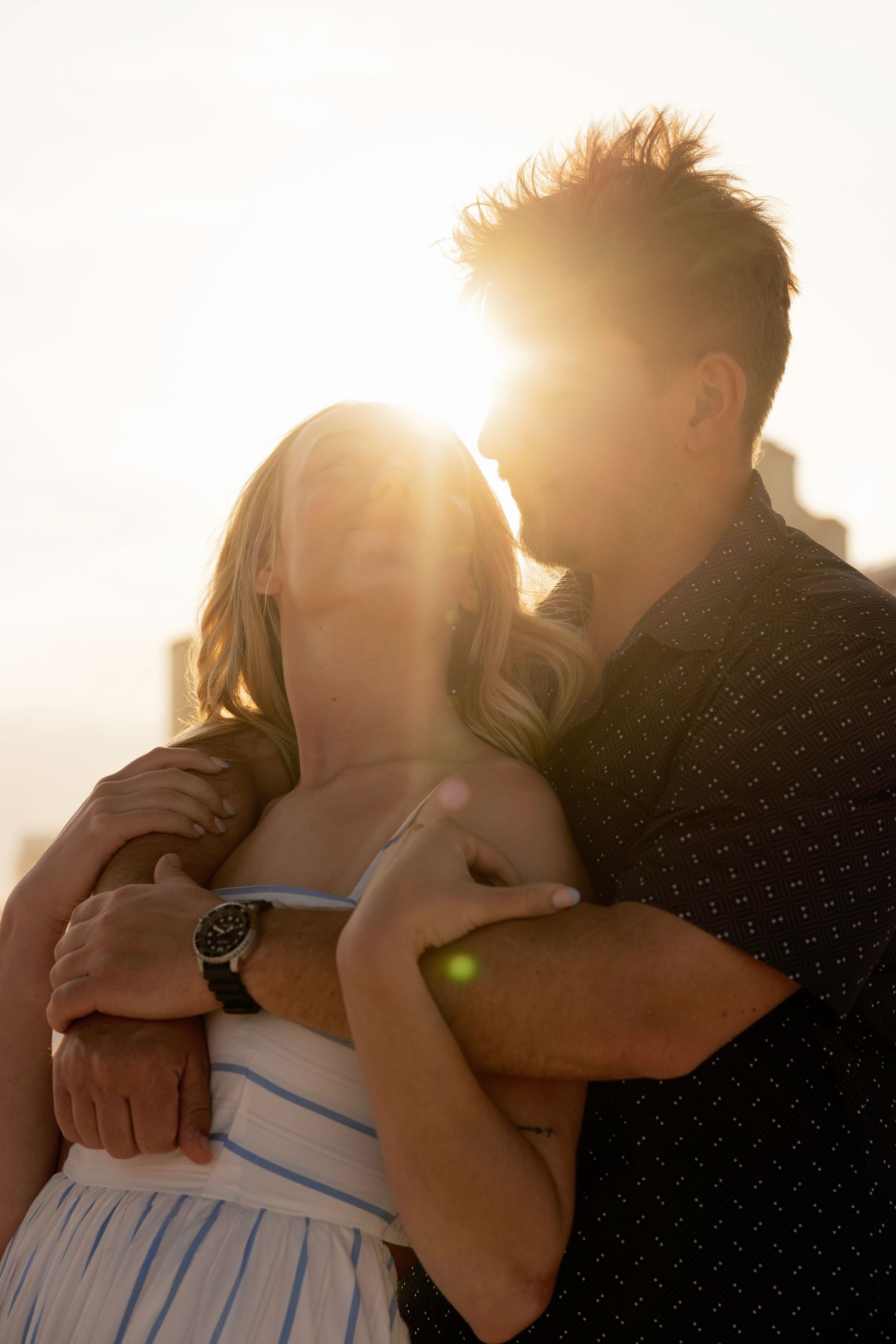 Romantic couple embracing at sunset on the beach, backlit by golden sunlight in a warm glow.