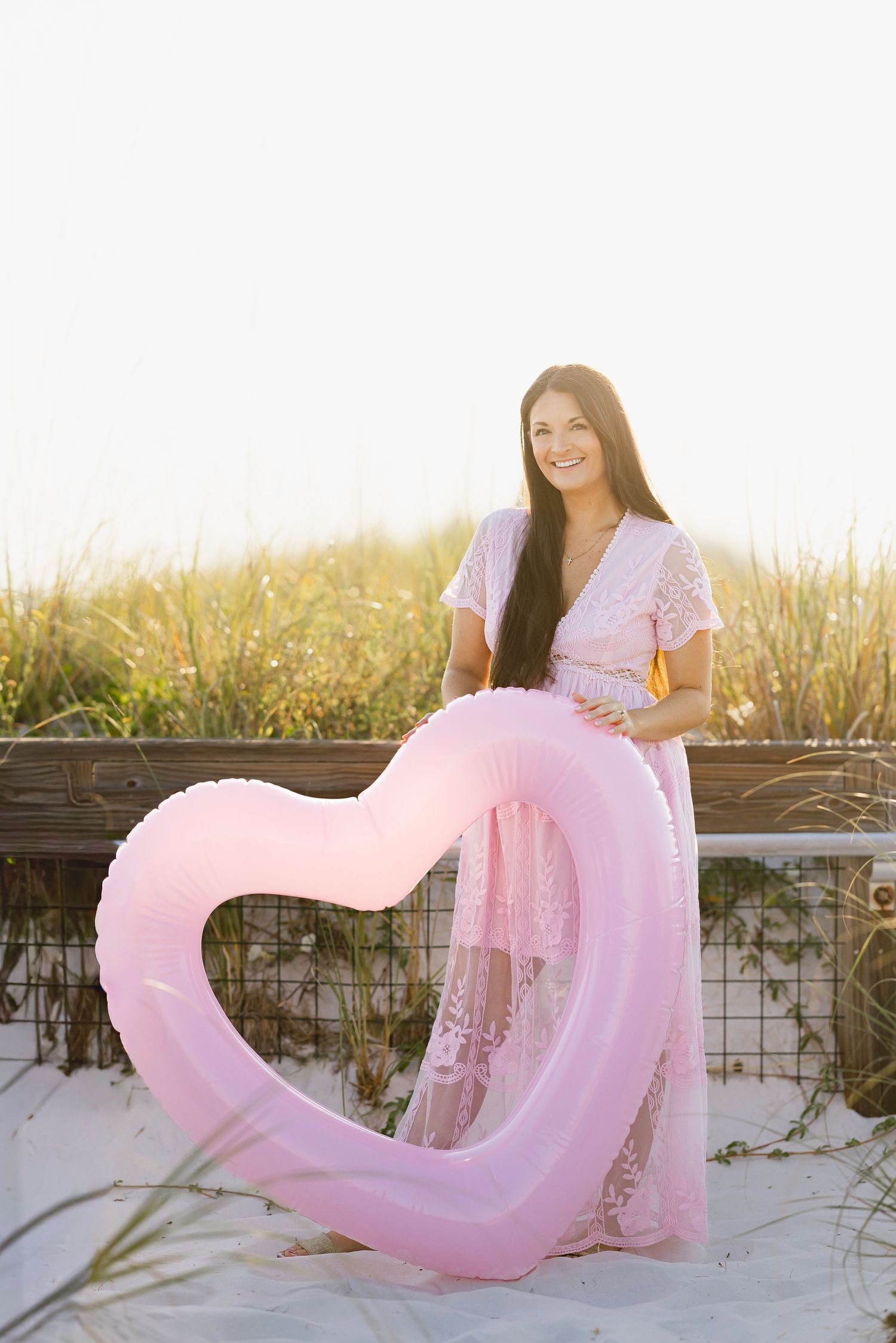 A pink dress flows gracefully in the breeze against a beach fence during golden hour.