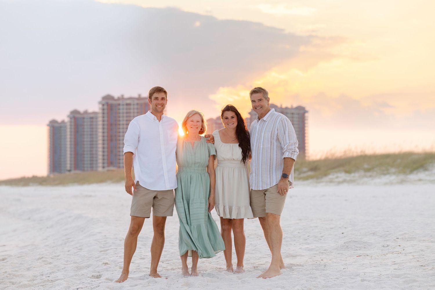 Family group dressed in coordinated beach outfits walking along sandy shoreline at sunset.