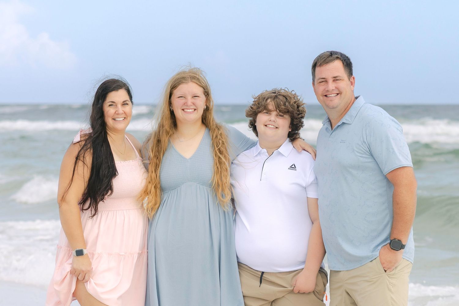 A group of people wearing coordinated blue and white outfits pose together on a sunny beach.