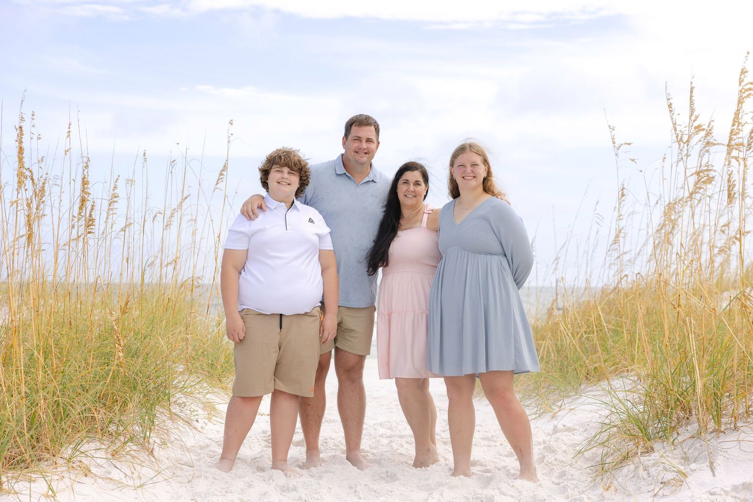 Family members stand together on beach path with tall grass and ocean view.