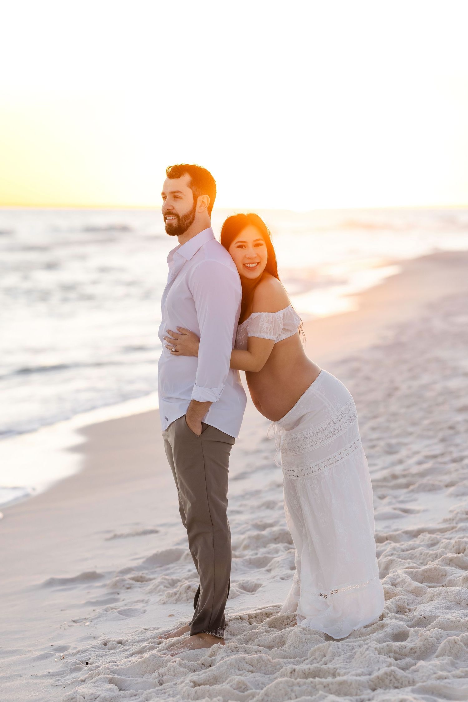 A romantic couple embraces on a sandy beach at sunset during their wedding photoshoot.