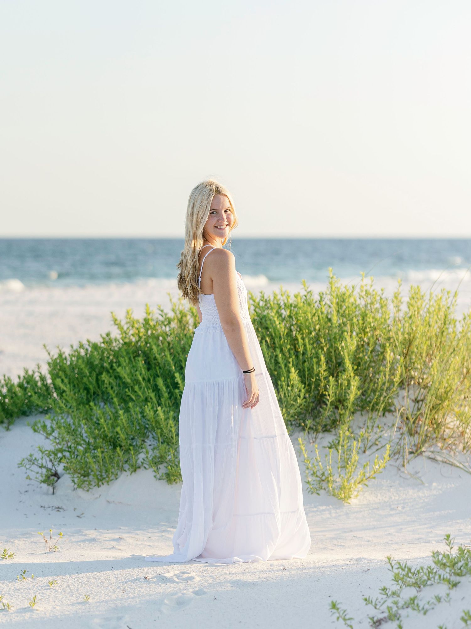A series of photos showing a person in a flowing white dress standing among beach dunes at sunset by the ocean.