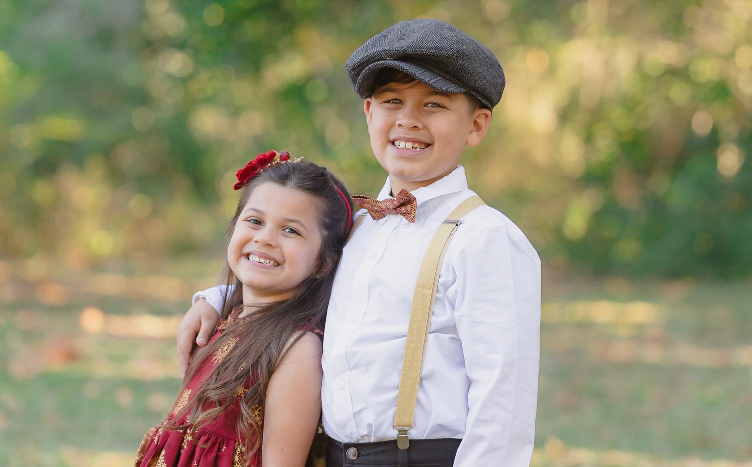 Children in traditional clothing sit together on rustic wooden steps surrounded by greenery and autumn leaves.