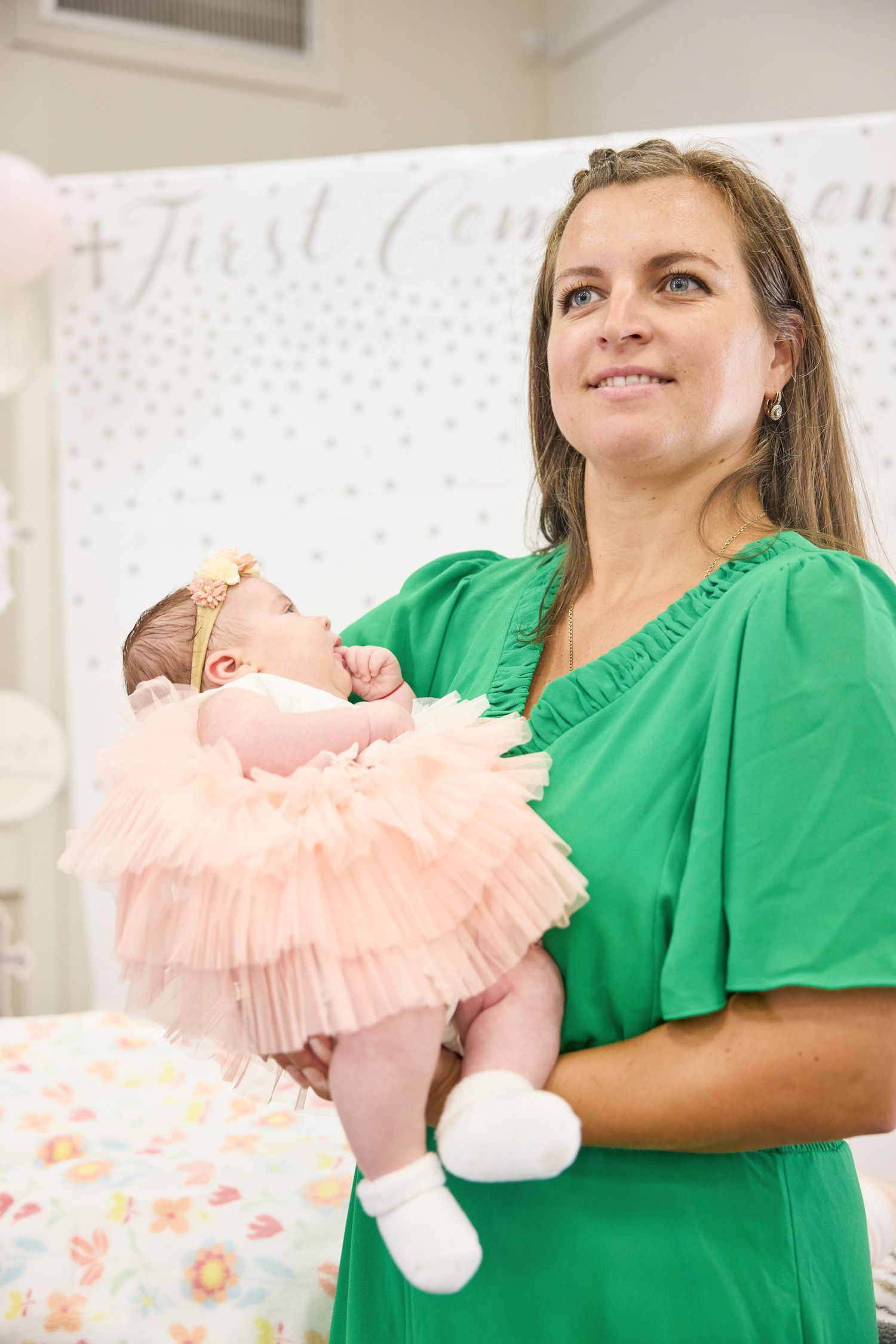 Healthcare worker in green scrubs holds a newborn baby wearing a pink ruffled outfit in a medical setting.