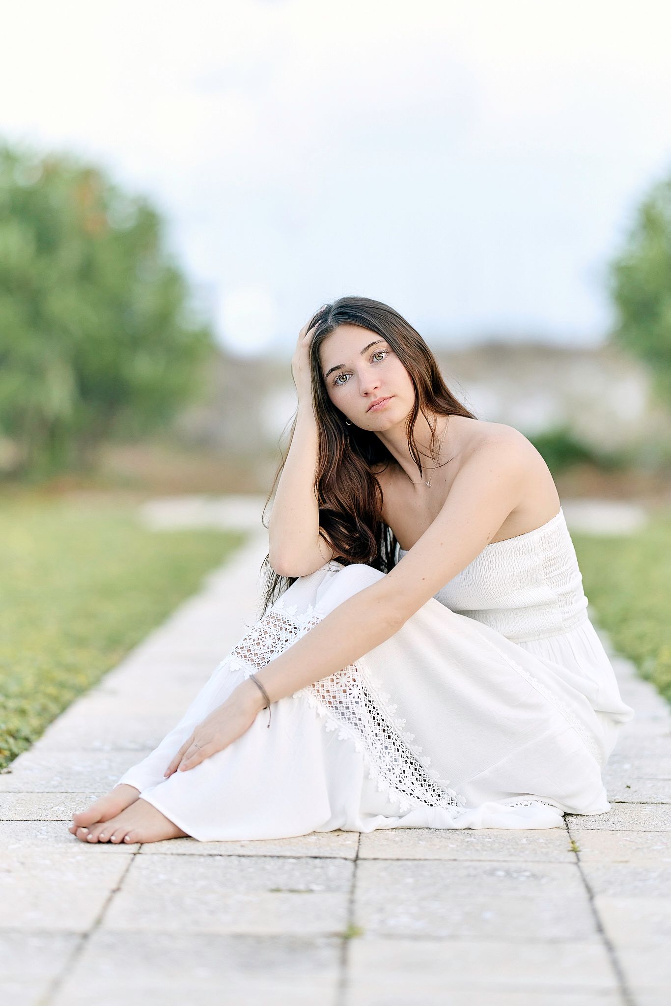 Outdoor portrait in white lace dress sitting on stone pavers.