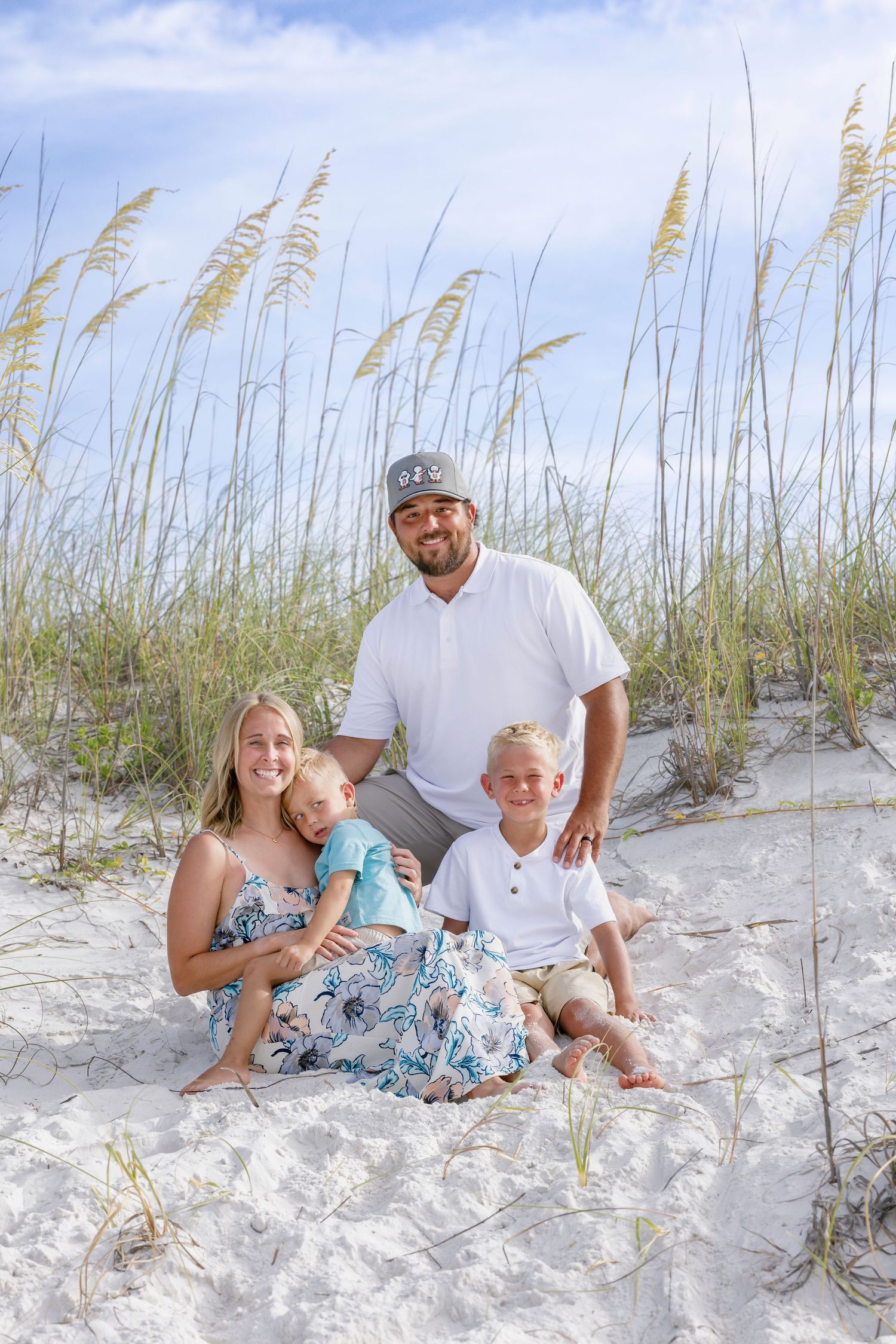 Happy family of four sitting in sandy beach dunes surrounded by sea oats grass.
