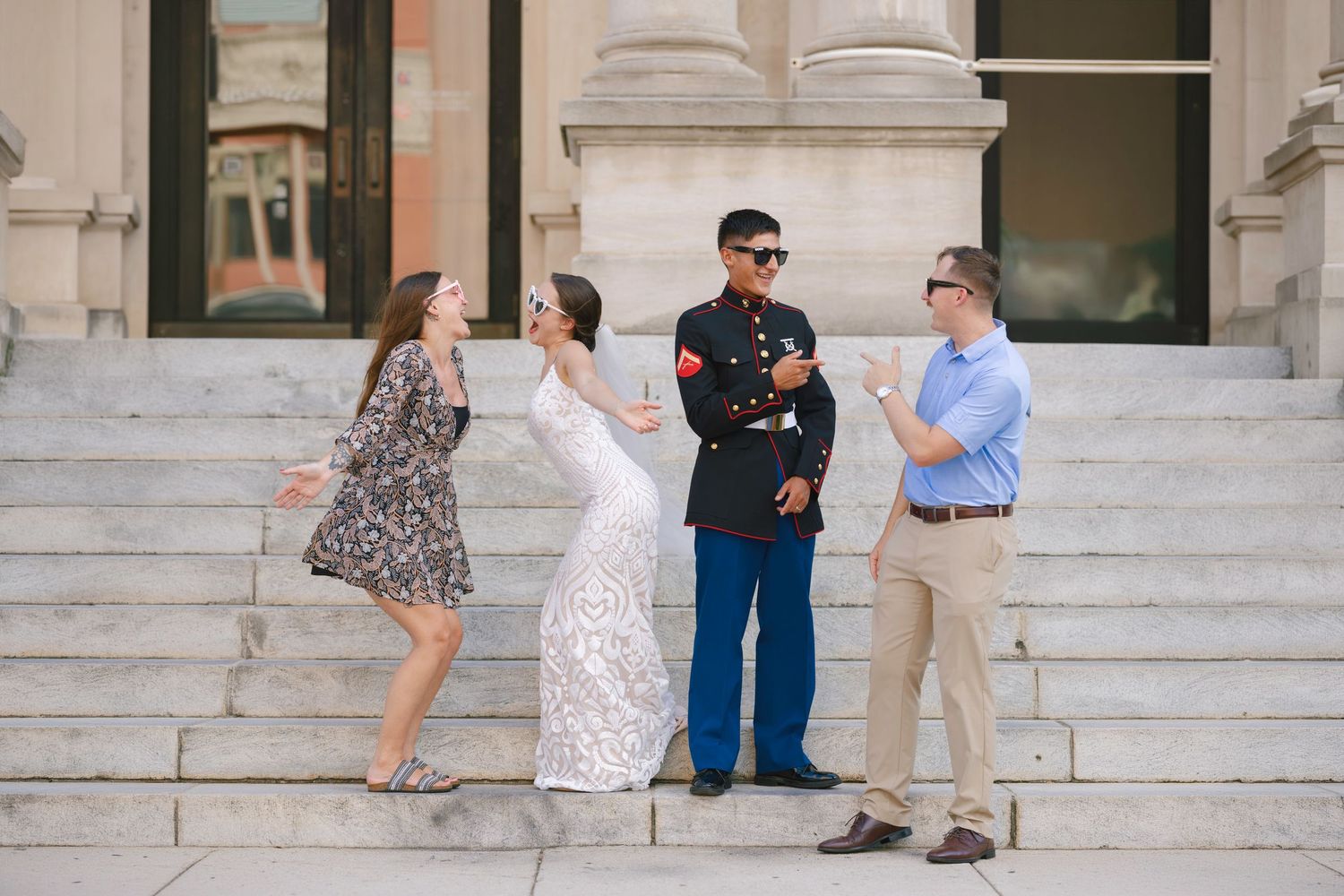 Bride in white gown and Marine in dress uniform pose with two guests on building steps.