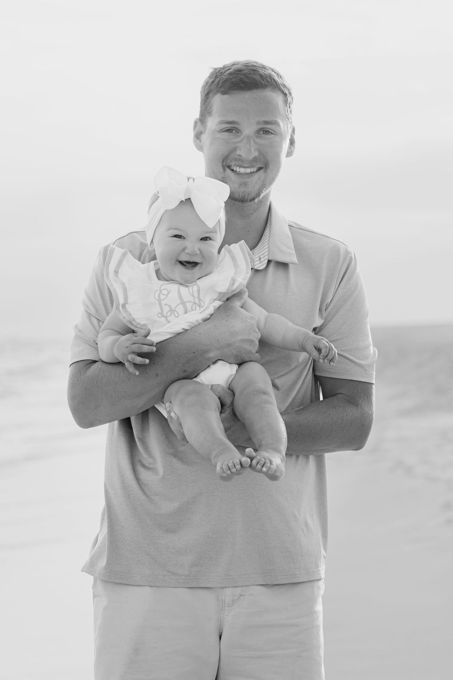Happy father holding laughing baby girl on the beach in black and white portrait photo.