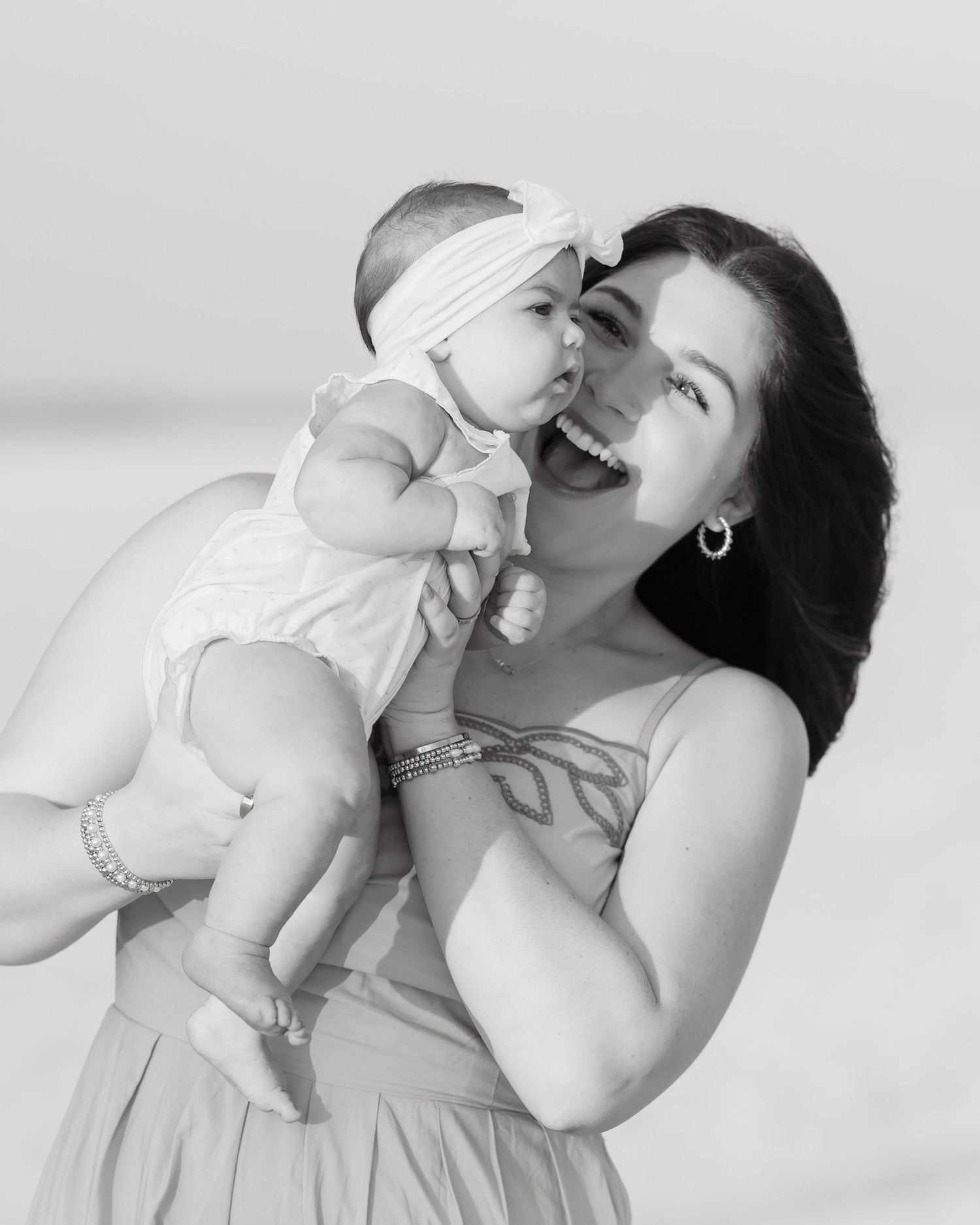 Black and white photo of a laughing woman holding a baby girl on a beach.