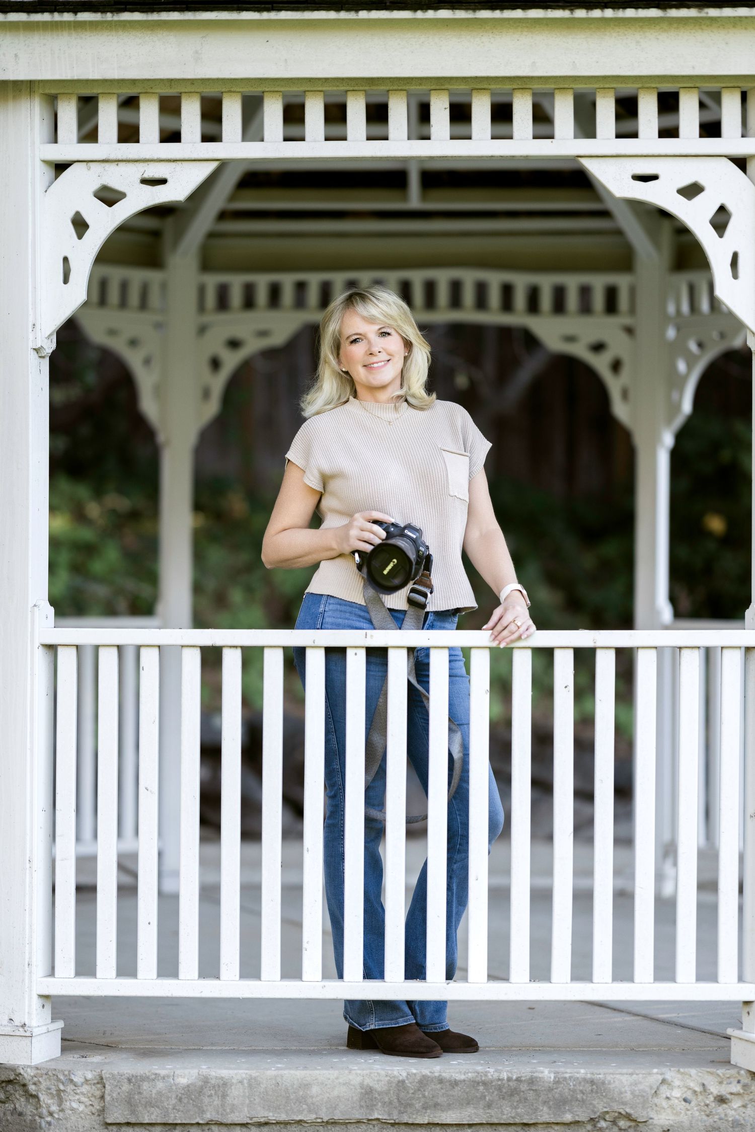 Professional photographer with camera stands in front of ornate white gazebo during outdoor photo session.