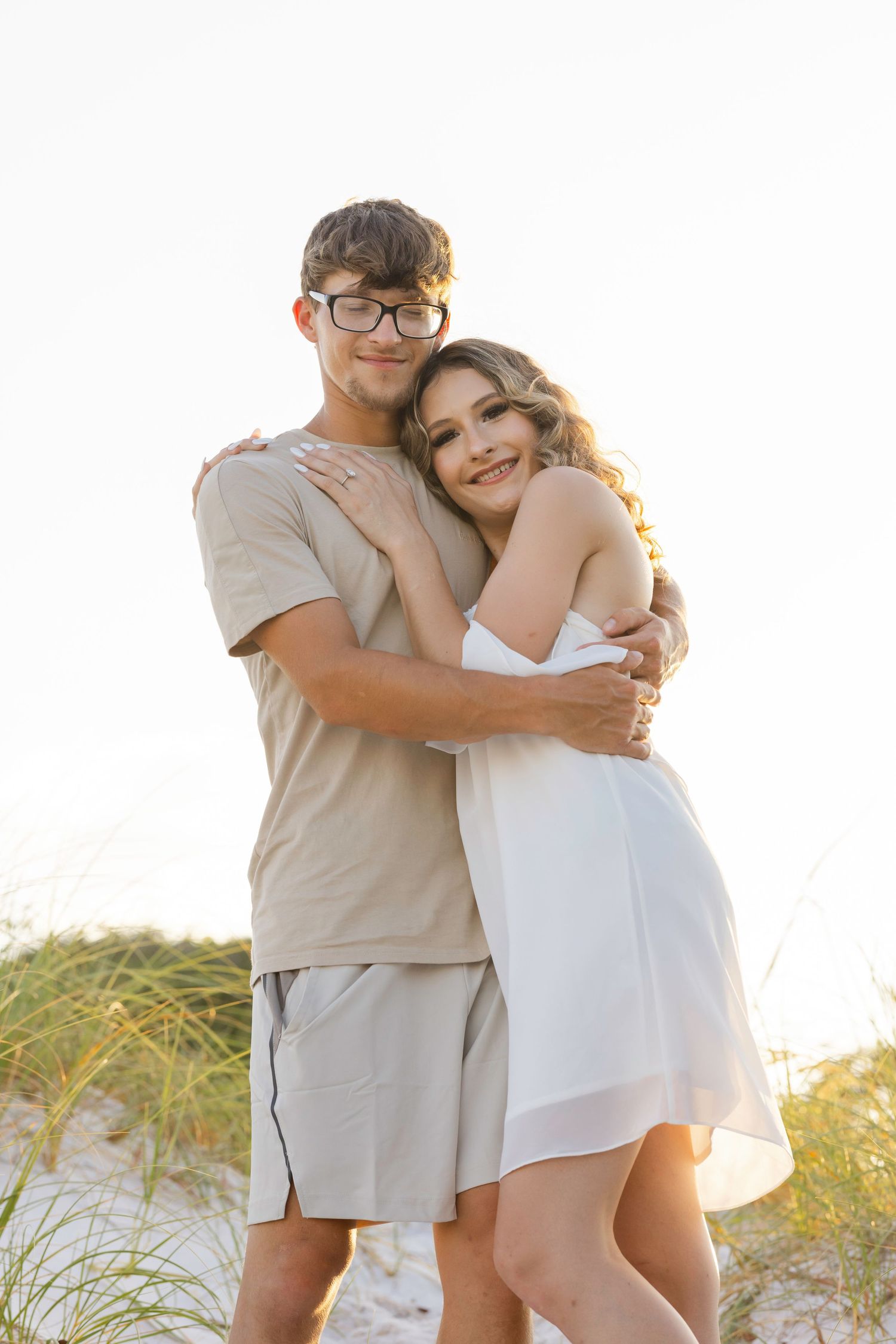 A romantic beach portrait of a couple embracing in casual summer outfits during golden hour.