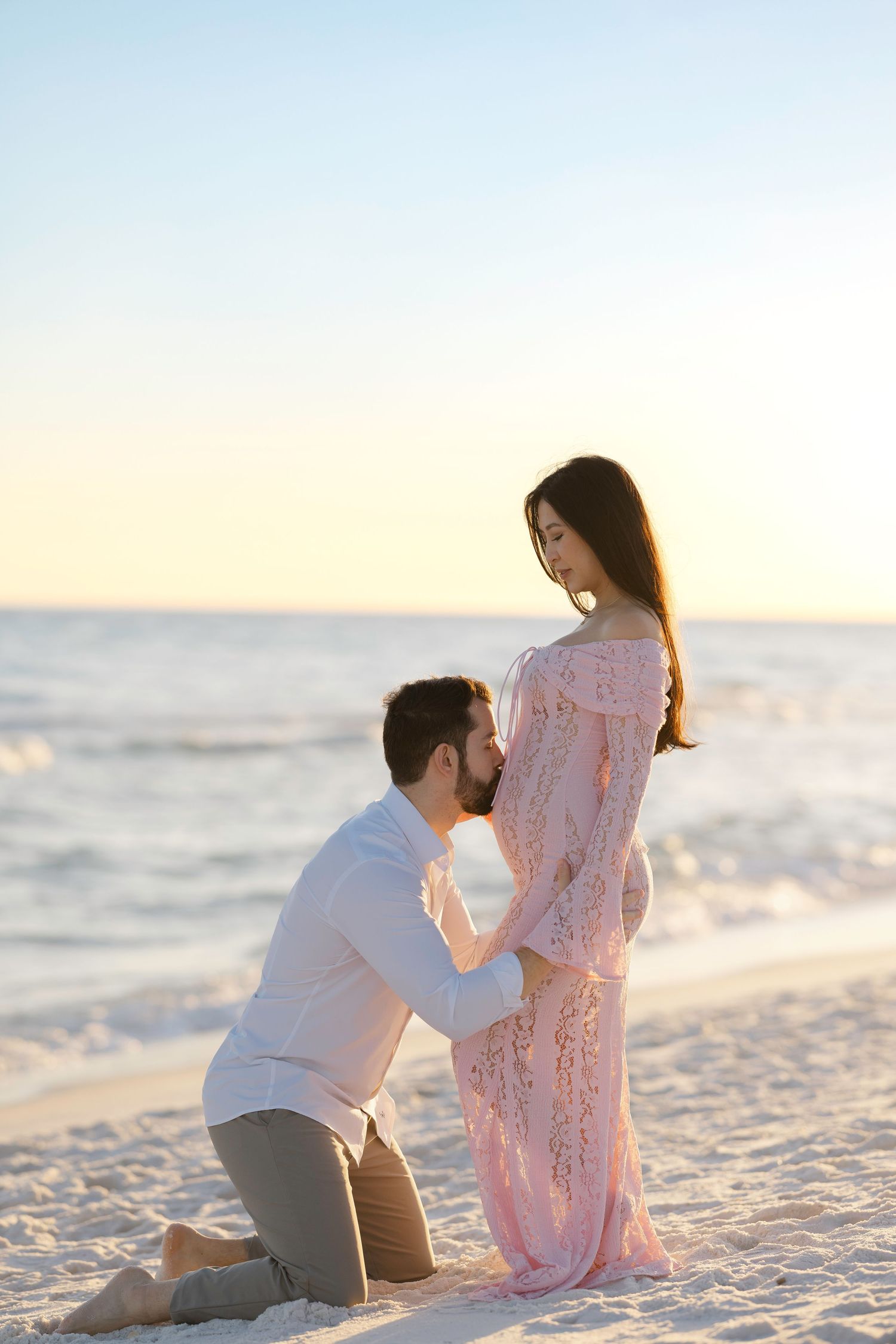 A couple sits together on a white sandy beach at sunset enjoying a romantic moment by the ocean.