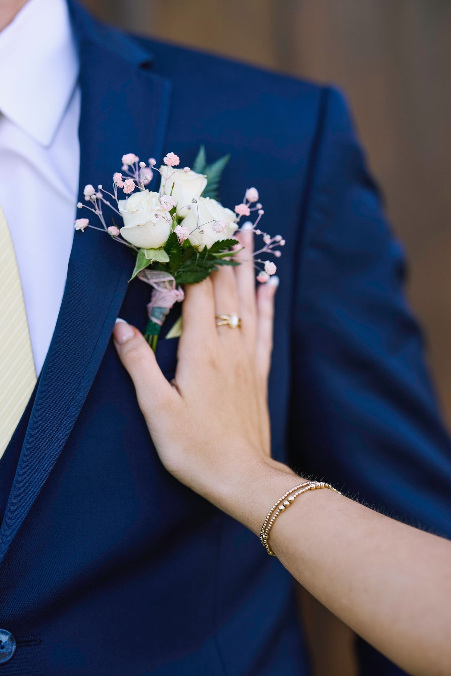 A close-up of a white rose and pink baby's breath boutonniere being pinned to a navy blue suit jacket.