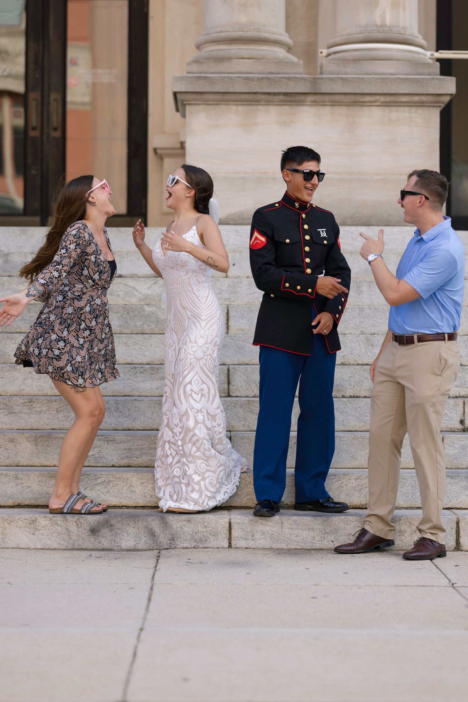 Marine in dress blues chats with family members on outdoor stone steps in sunlight.