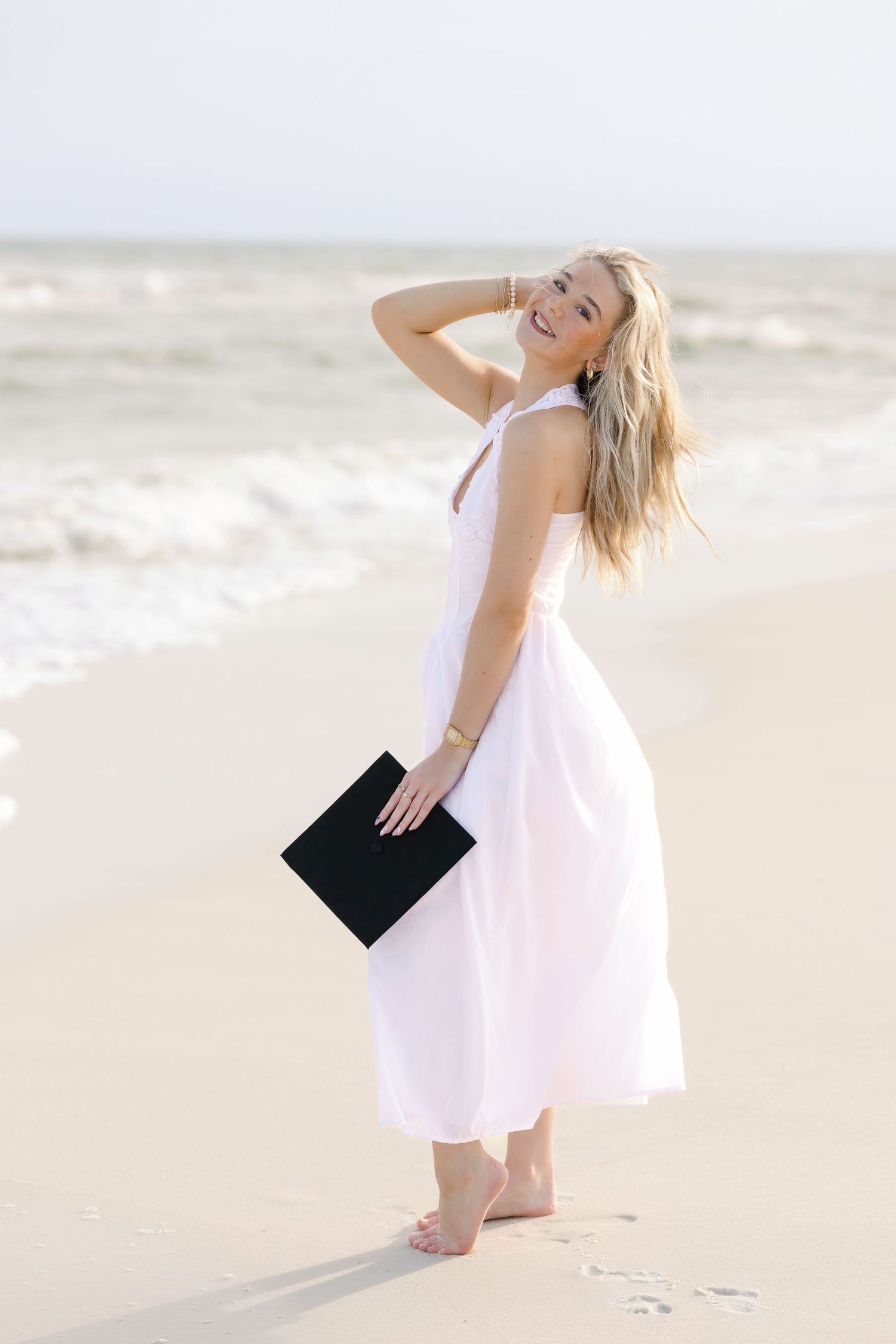 Figure in flowing white dress twirls elegantly on beach with ocean waves in background.