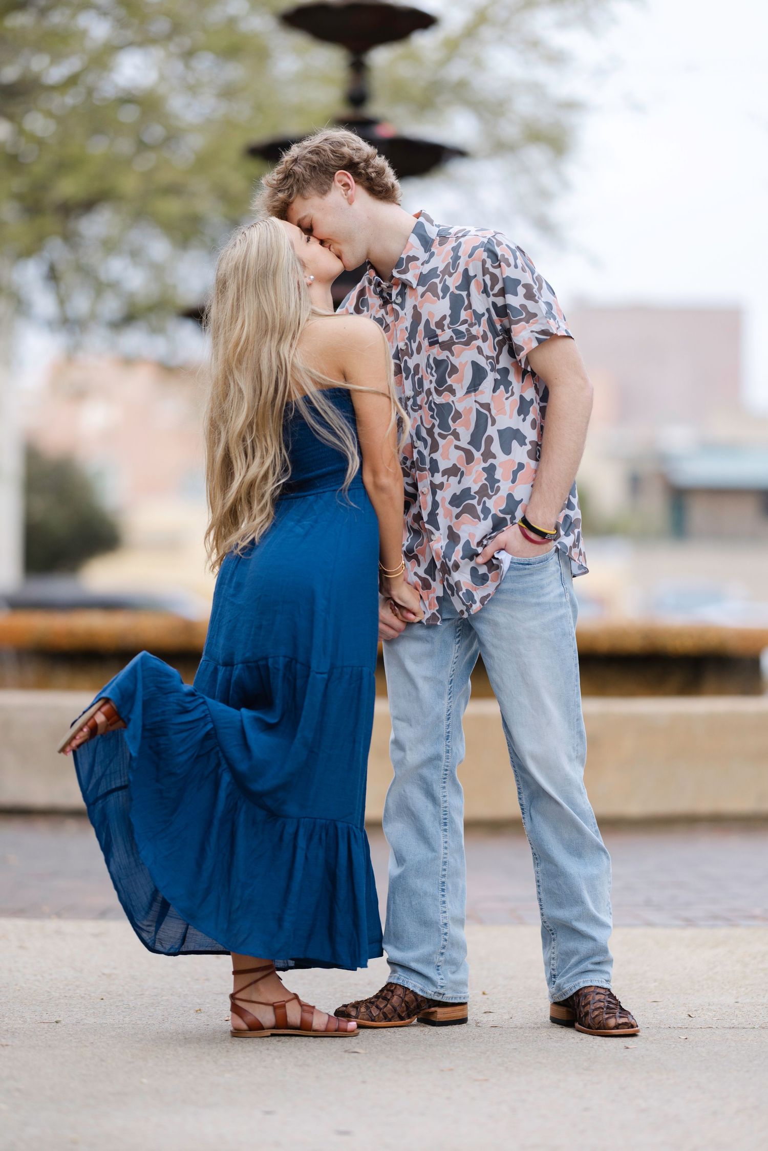 A couple poses together on stone steps with a blue dress and patterned shirt visible in the frame.