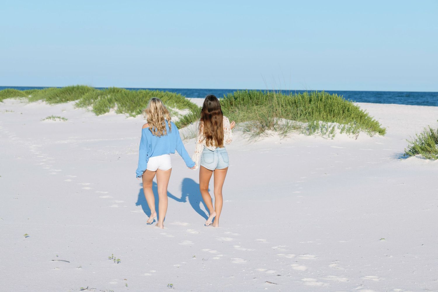 Two people walking together along white sandy beach with green dunes.