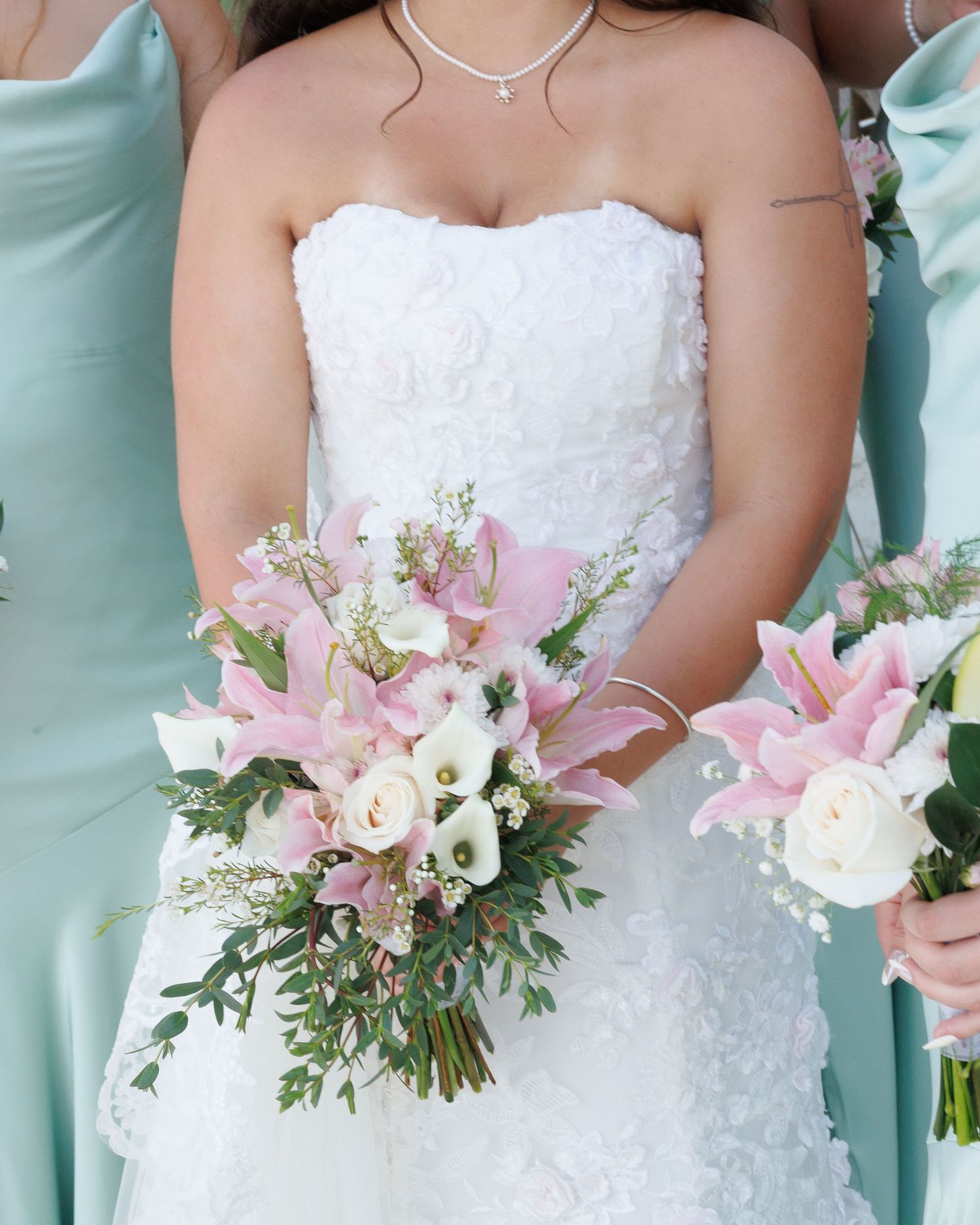 Close-up of bridal bouquet with pink lilies and white roses against white wedding dress.