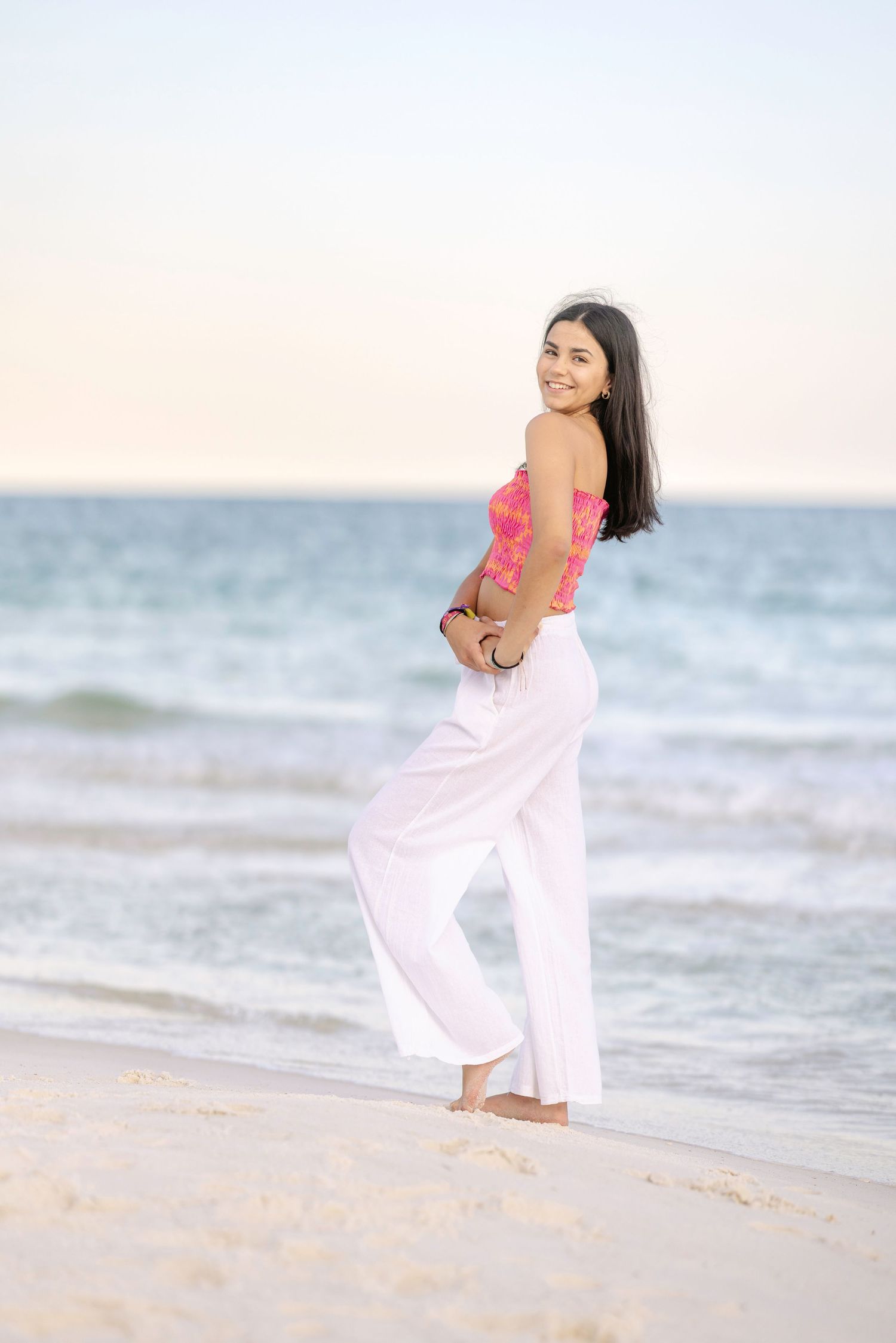 Playful movement shots on the beach with flowing white pants and coral top.