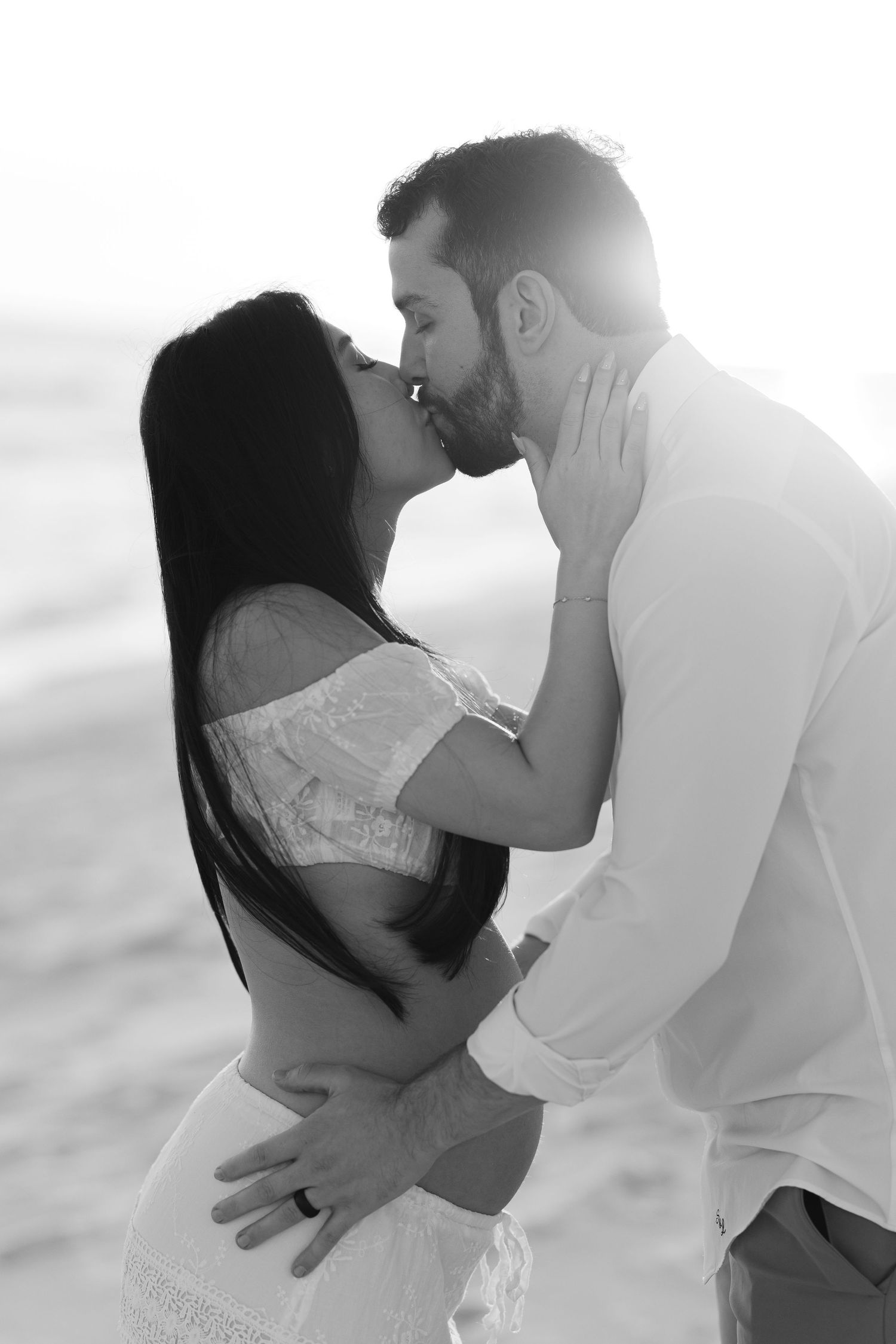 A romantic black and white photograph of a couple sharing an intimate kiss on a bright, hazy day.