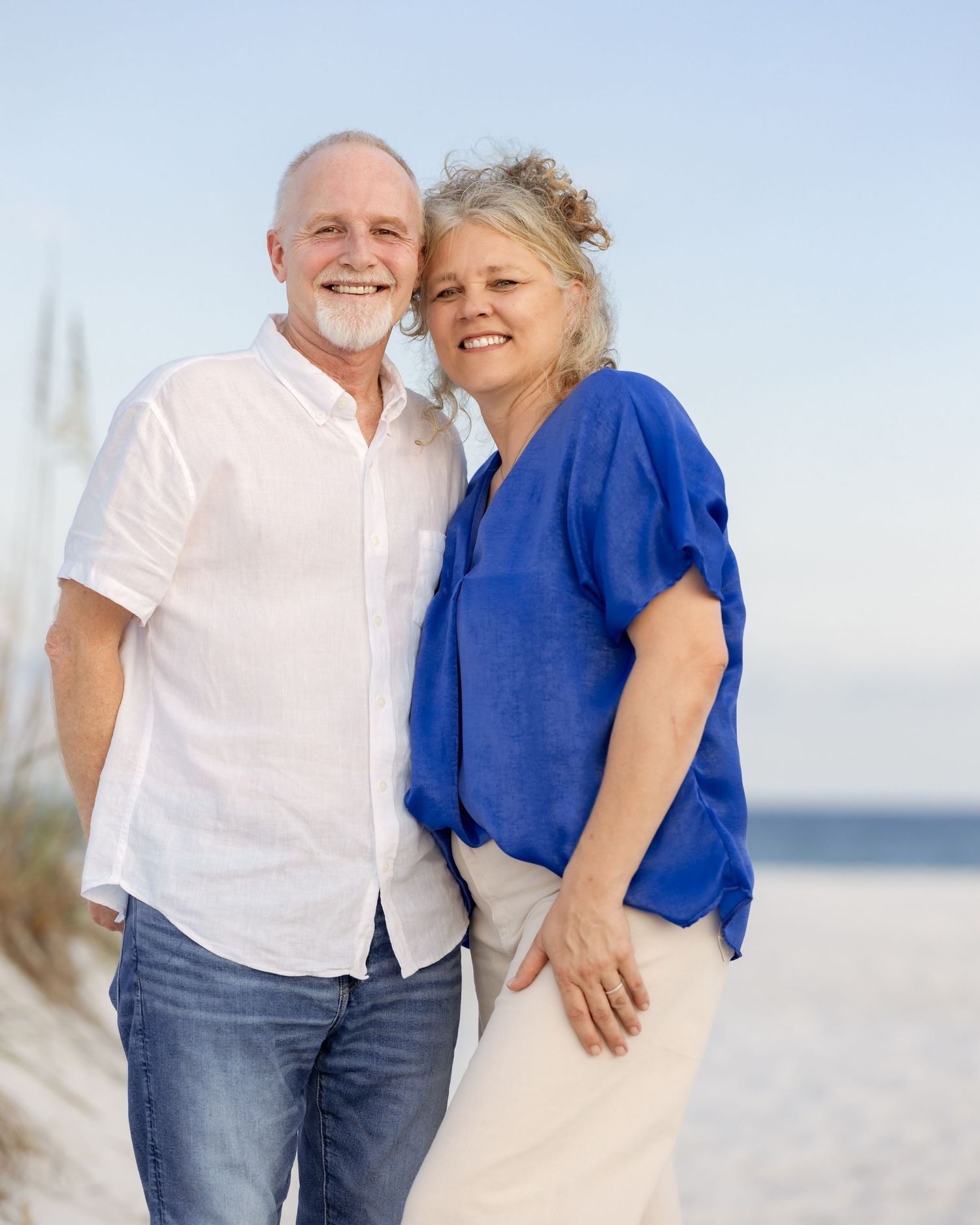 Happy mature couple posing together on sandy beach, woman in blue top and man in white shirt.