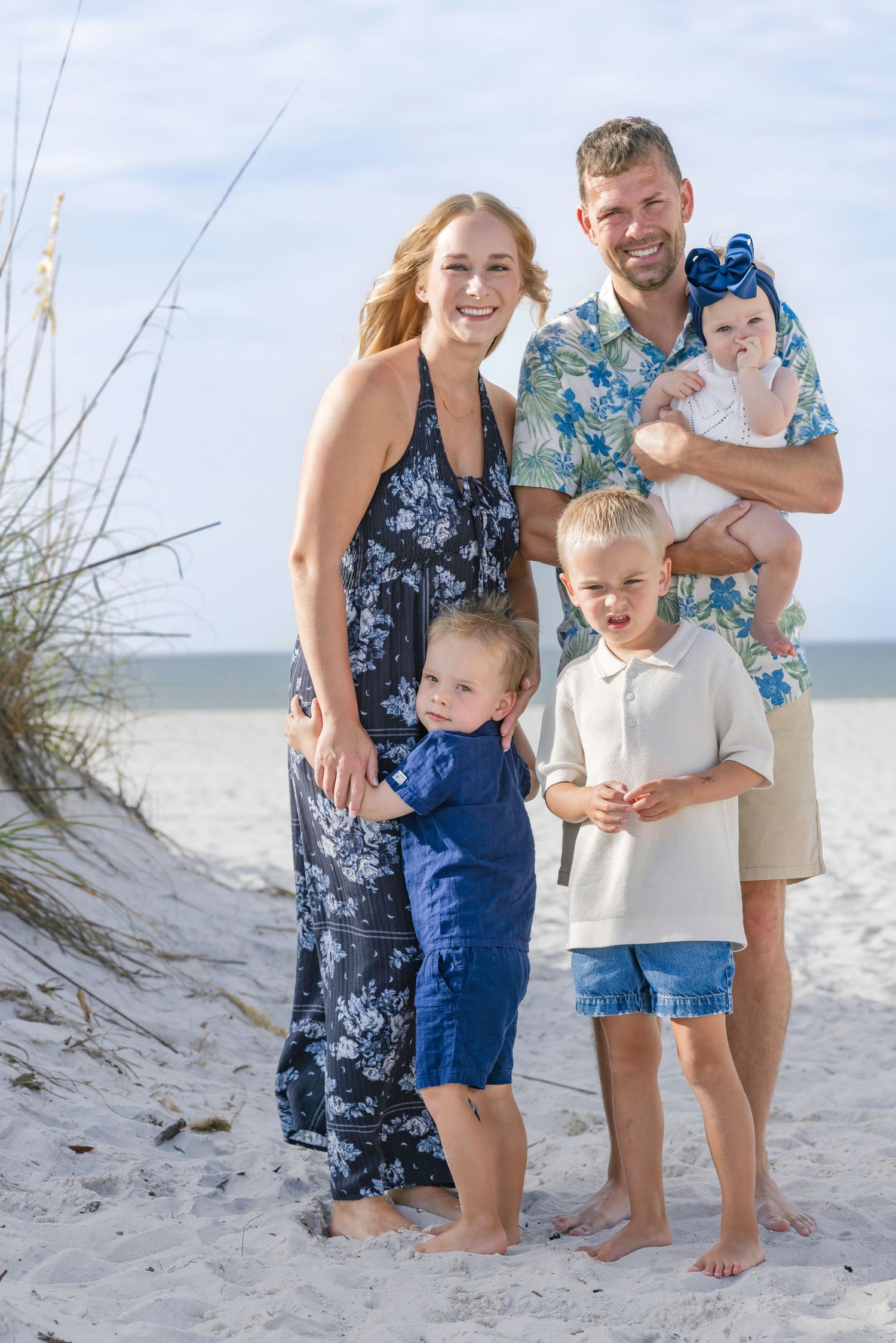 Happy family of five posing together on a sandy beach, parents with three young children on a sunny day.