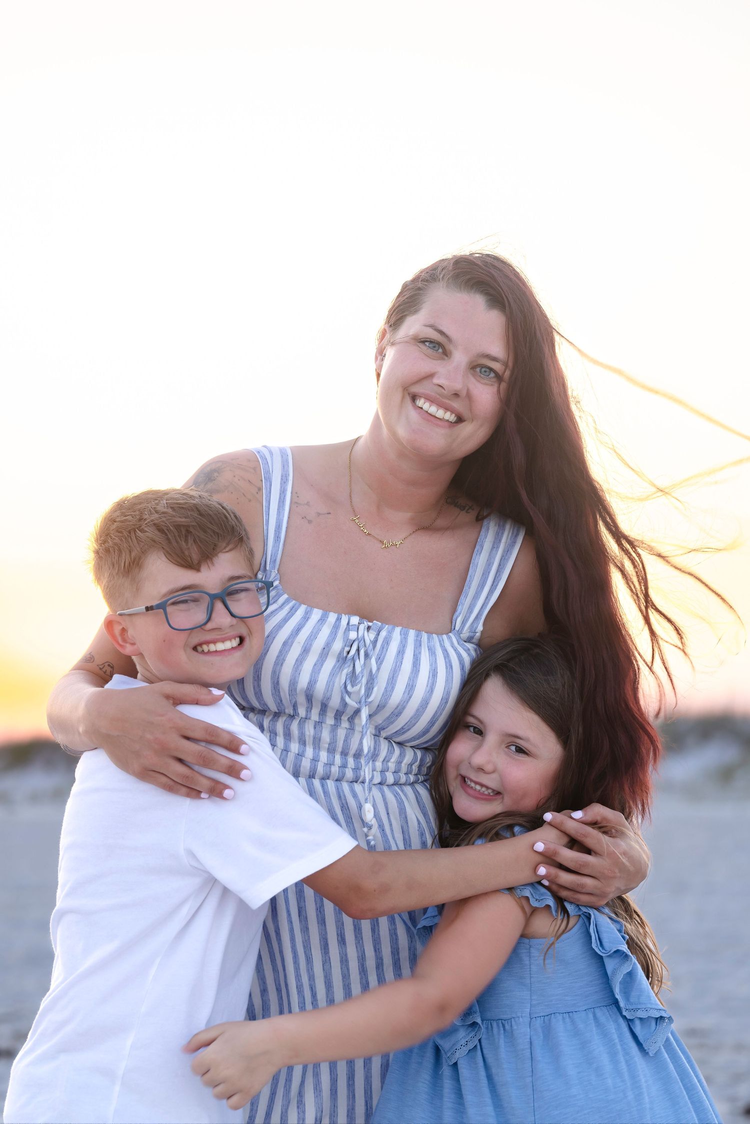 Smiling mother hugging her two children on a beach at golden sunset hour.