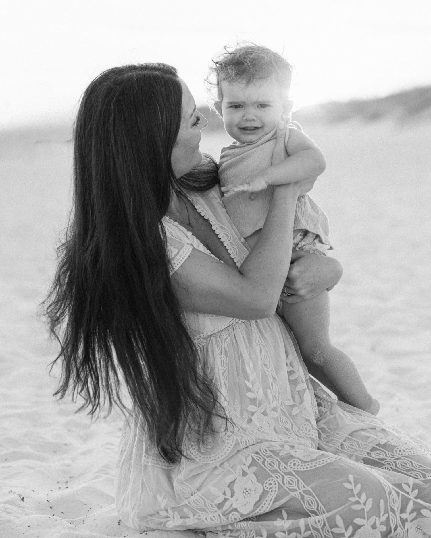 Black and white photo series showing tender moments between mother and baby playing together on the beach.