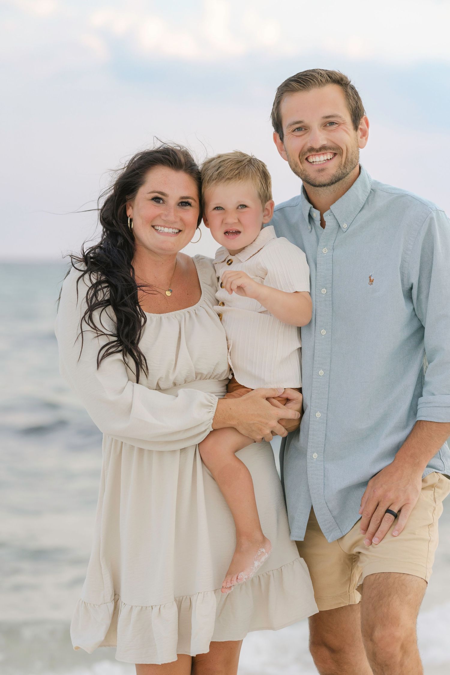 Family enjoys a sunset photo session together on a white sand beach with ocean in background.