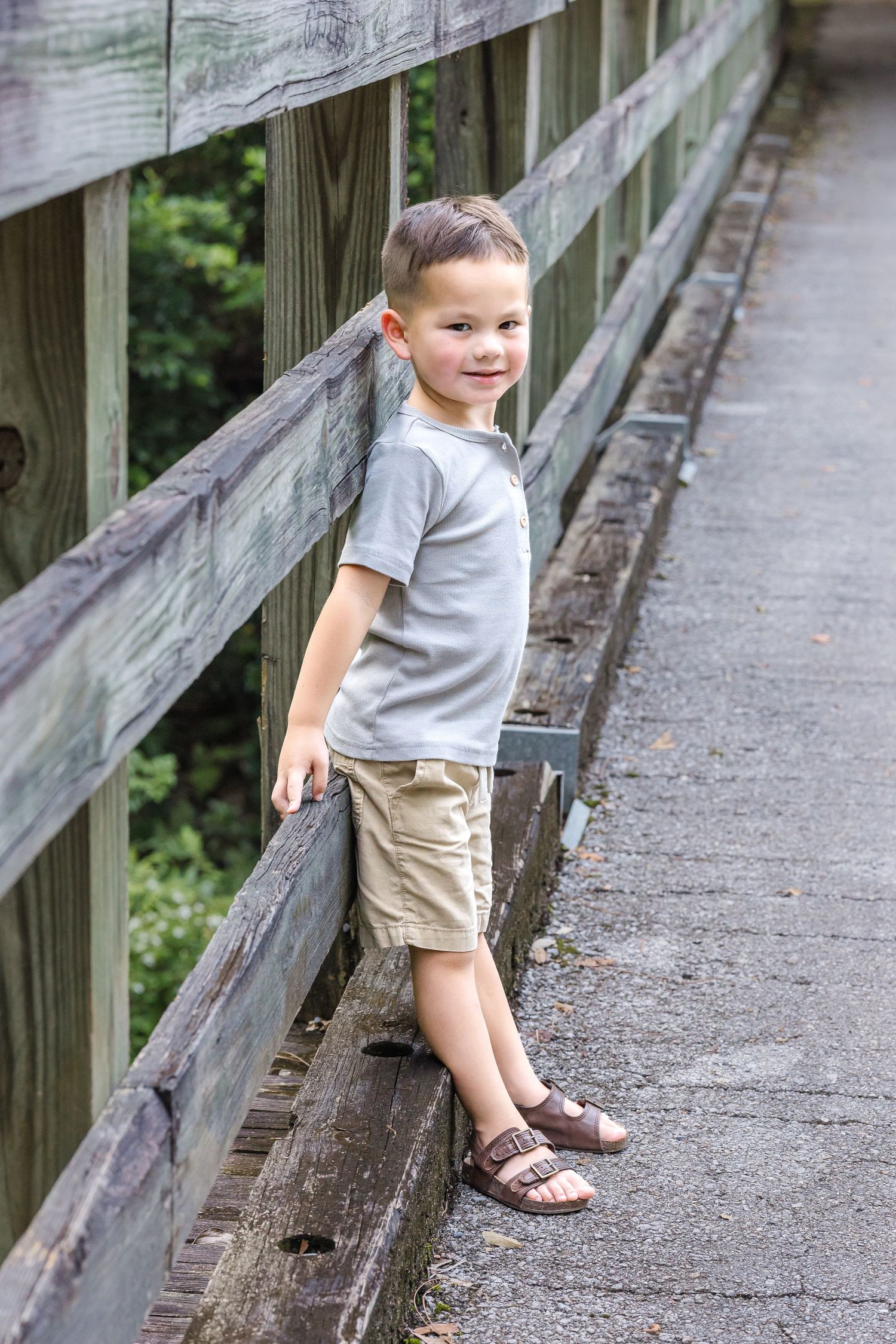 Small child in gray shirt and tan shorts playing on a wooden boardwalk railing.