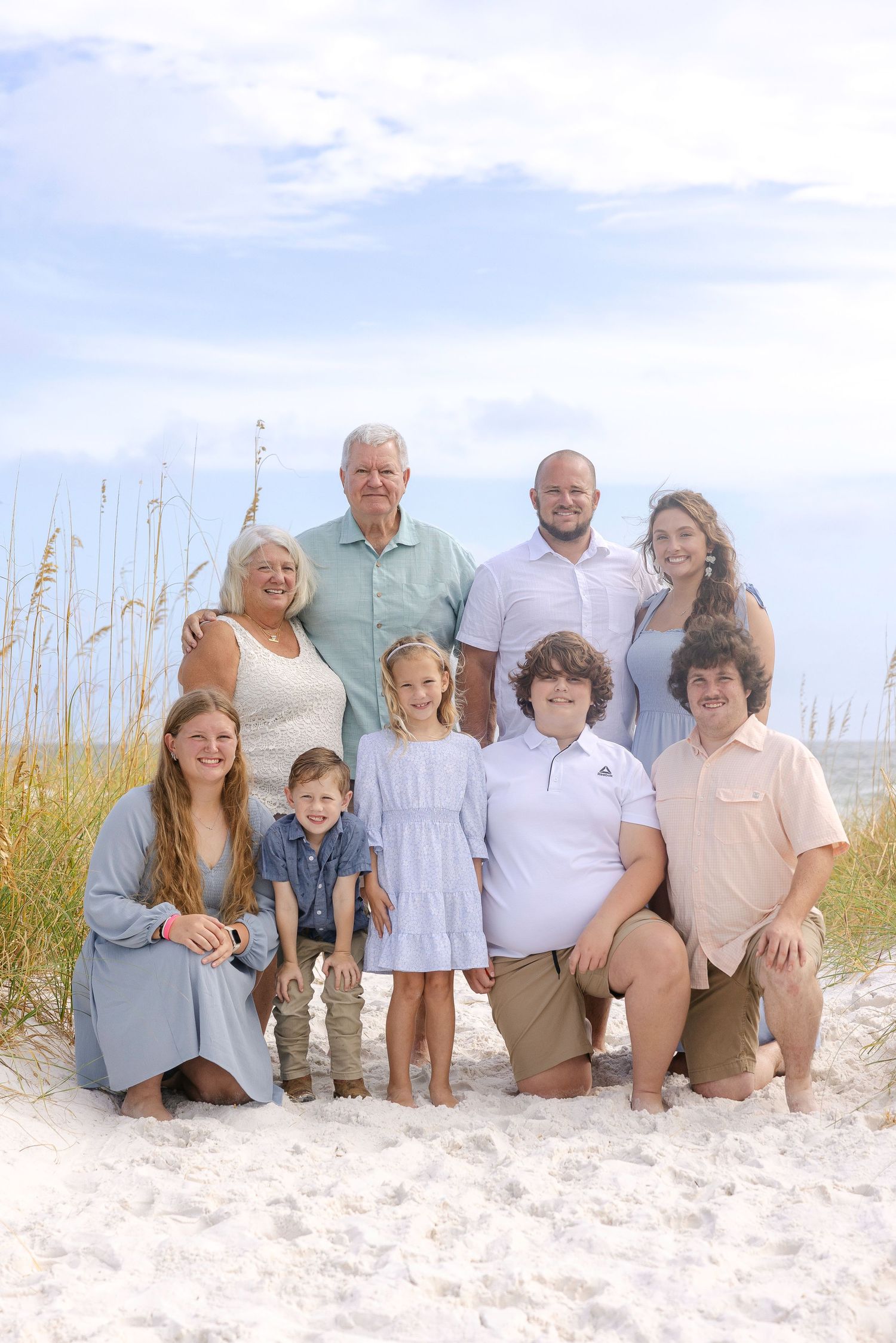 Extended family poses together on white sandy beach with sea grass and ocean waves in background.