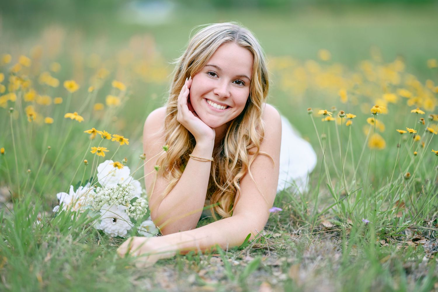 A portrait in a meadow with yellow wildflowers and white bouquet on a sunny day.