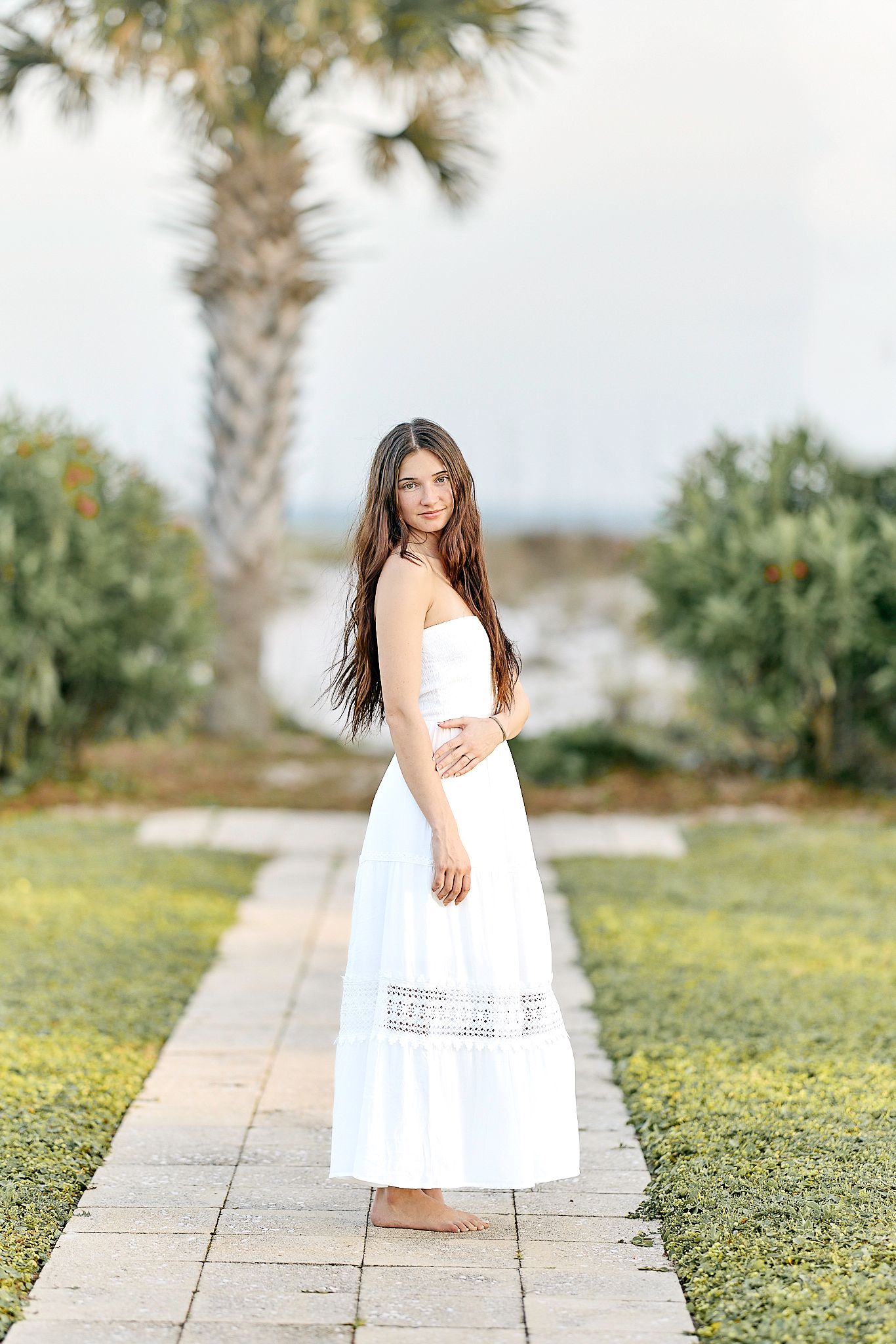 White sundress stands out against palm trees and garden path in coastal photography.