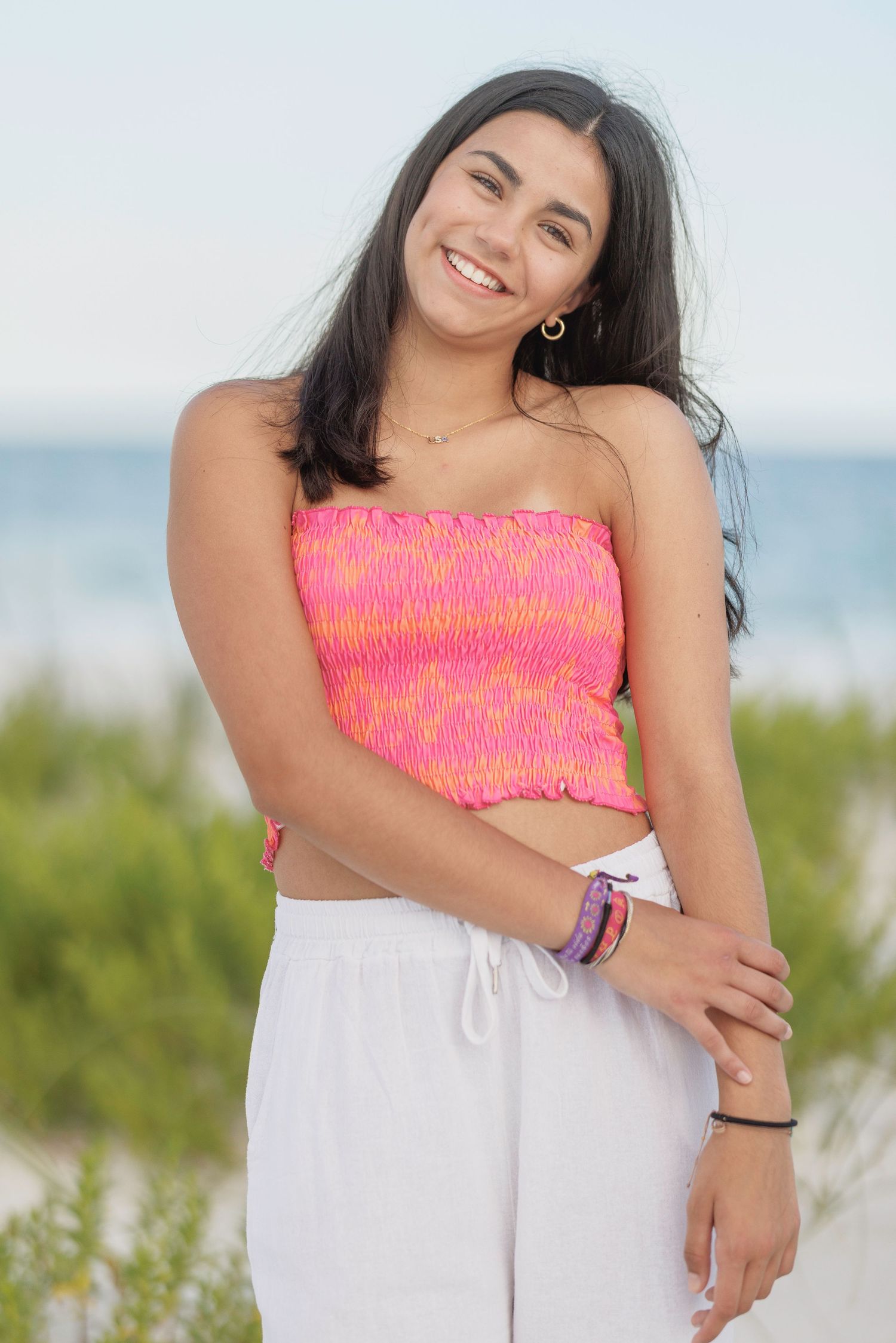 Bright pink smocked top paired with white pants in beachside summer portrait.