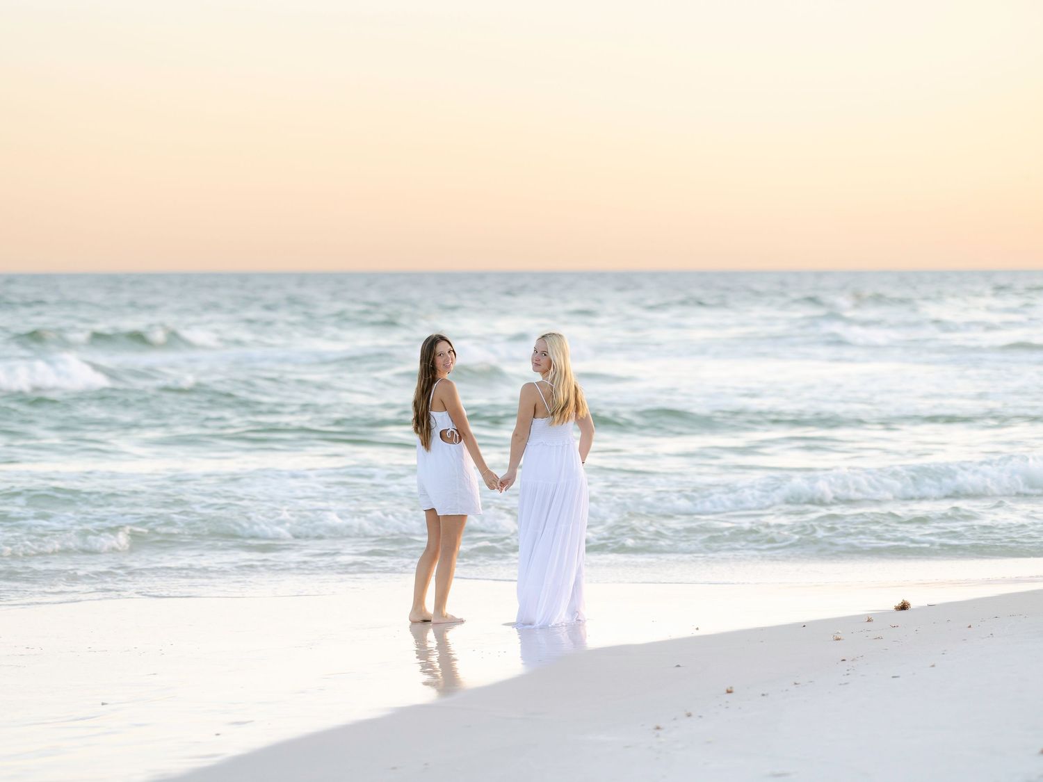 Two people walking together on sandy beach with waves breaking behind them.