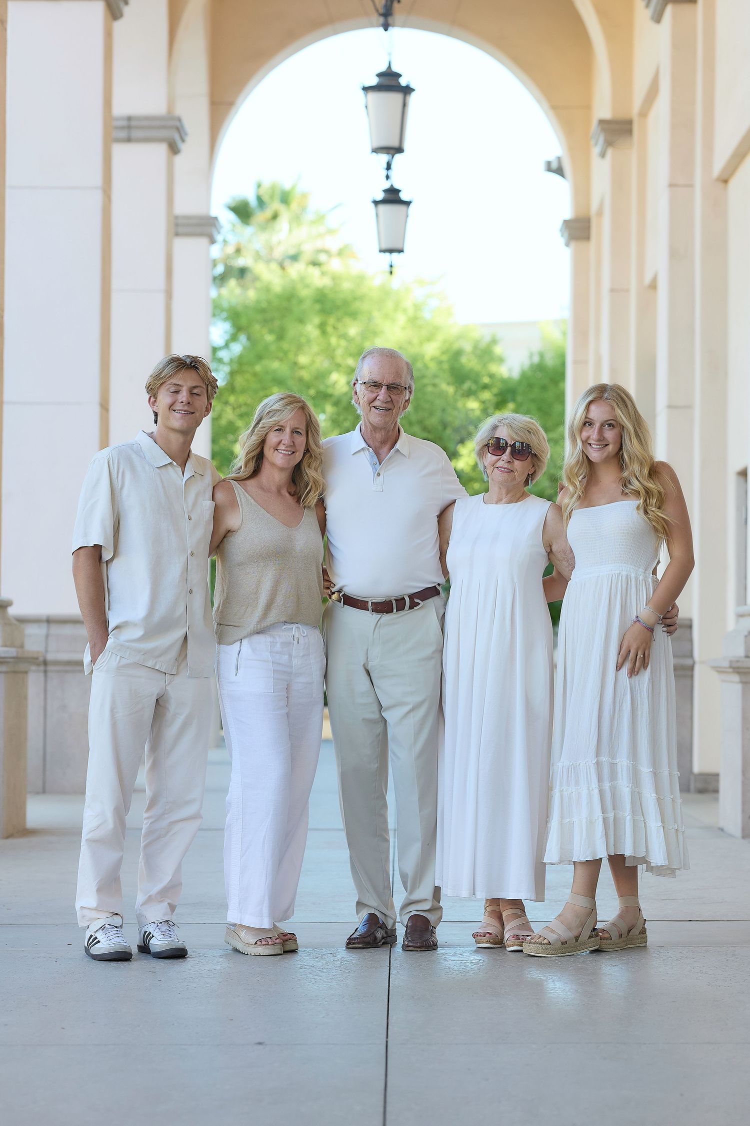 Family group wearing coordinated white and beige outfits poses together in an elegant covered colonnade with lanterns.