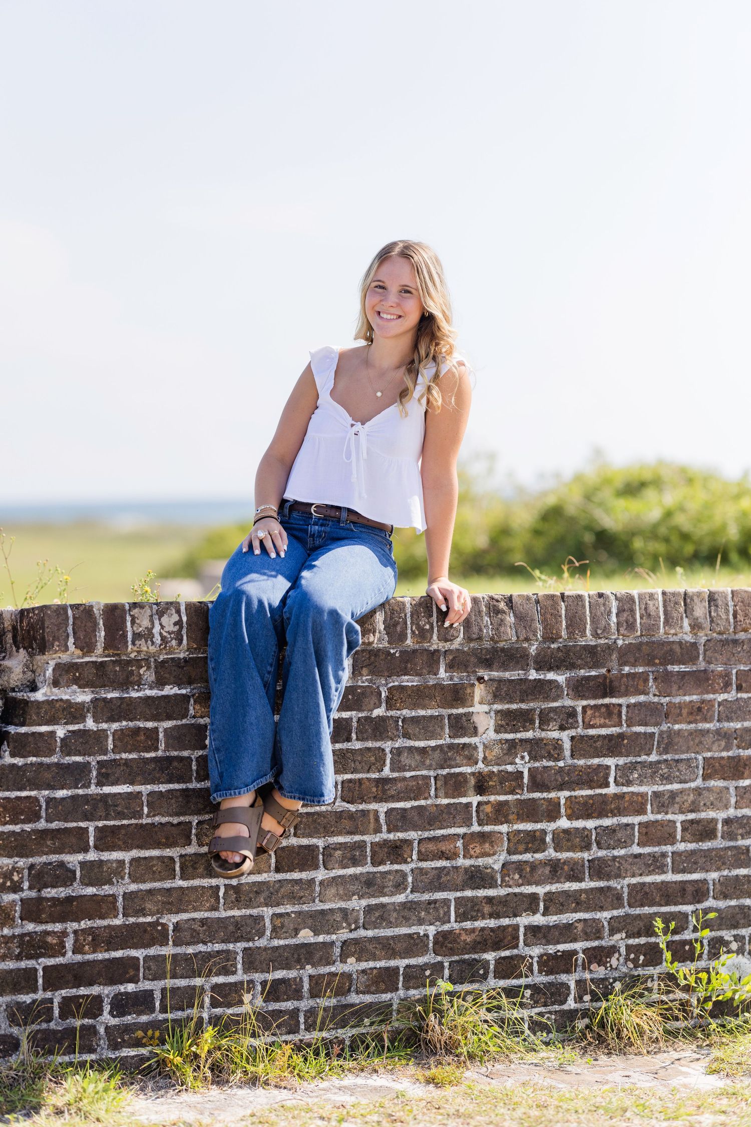 A casual portrait series showing someone sitting on a rustic brick wall in blue jeans on a sunny day.