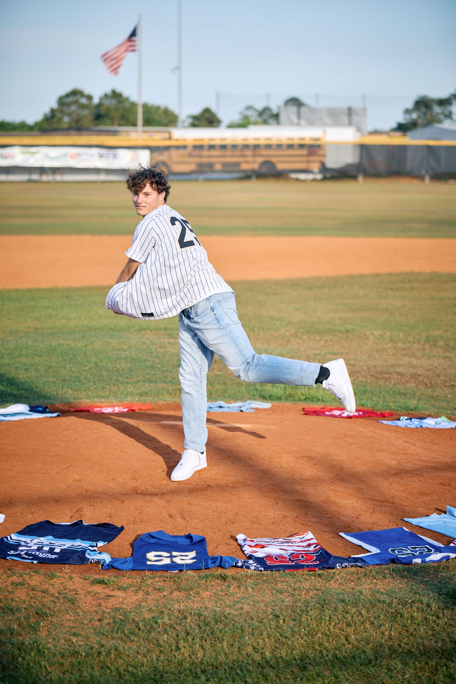 Baseball player in pinstripes practices pitching form on field with jerseys laid out on grass.