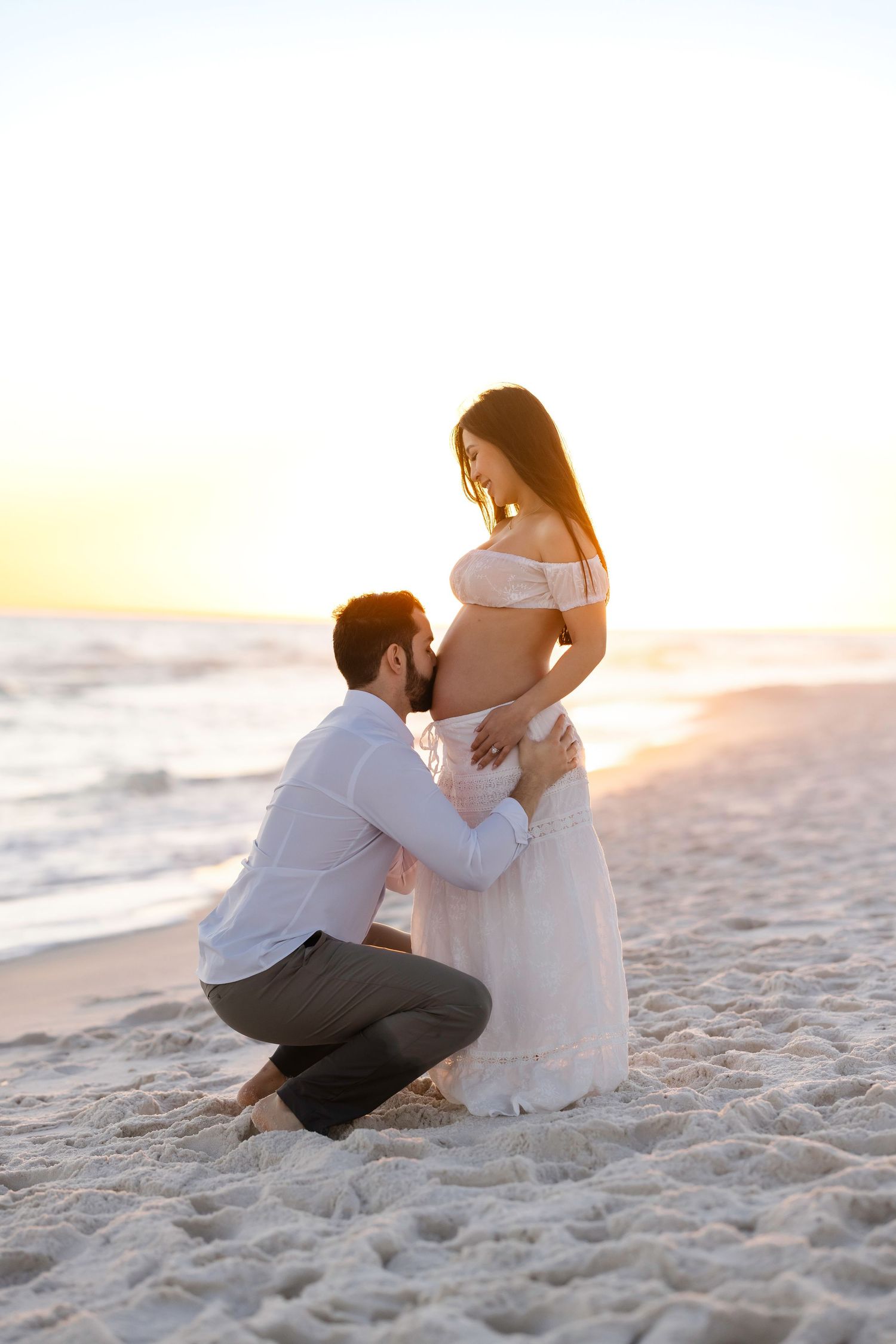 Couple shares tender moment during beach maternity photoshoot at dusk.