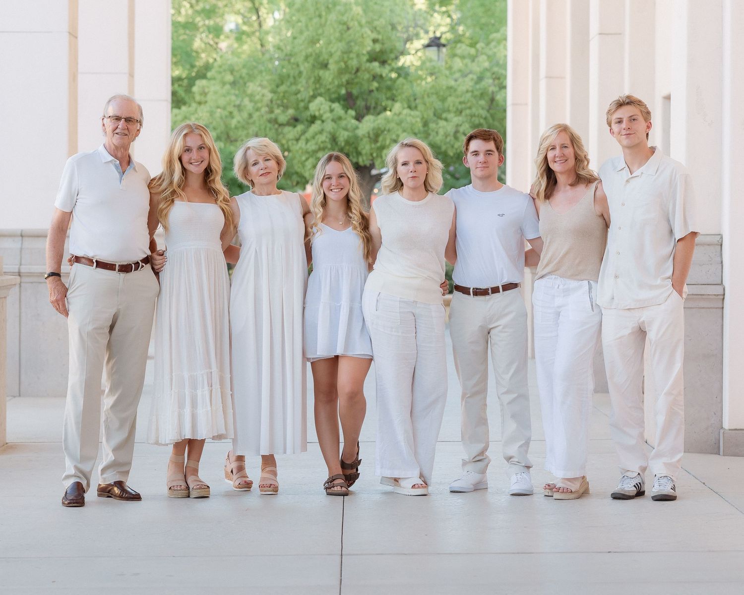 Large family of eight poses together in coordinated white and neutral outfits outdoors.